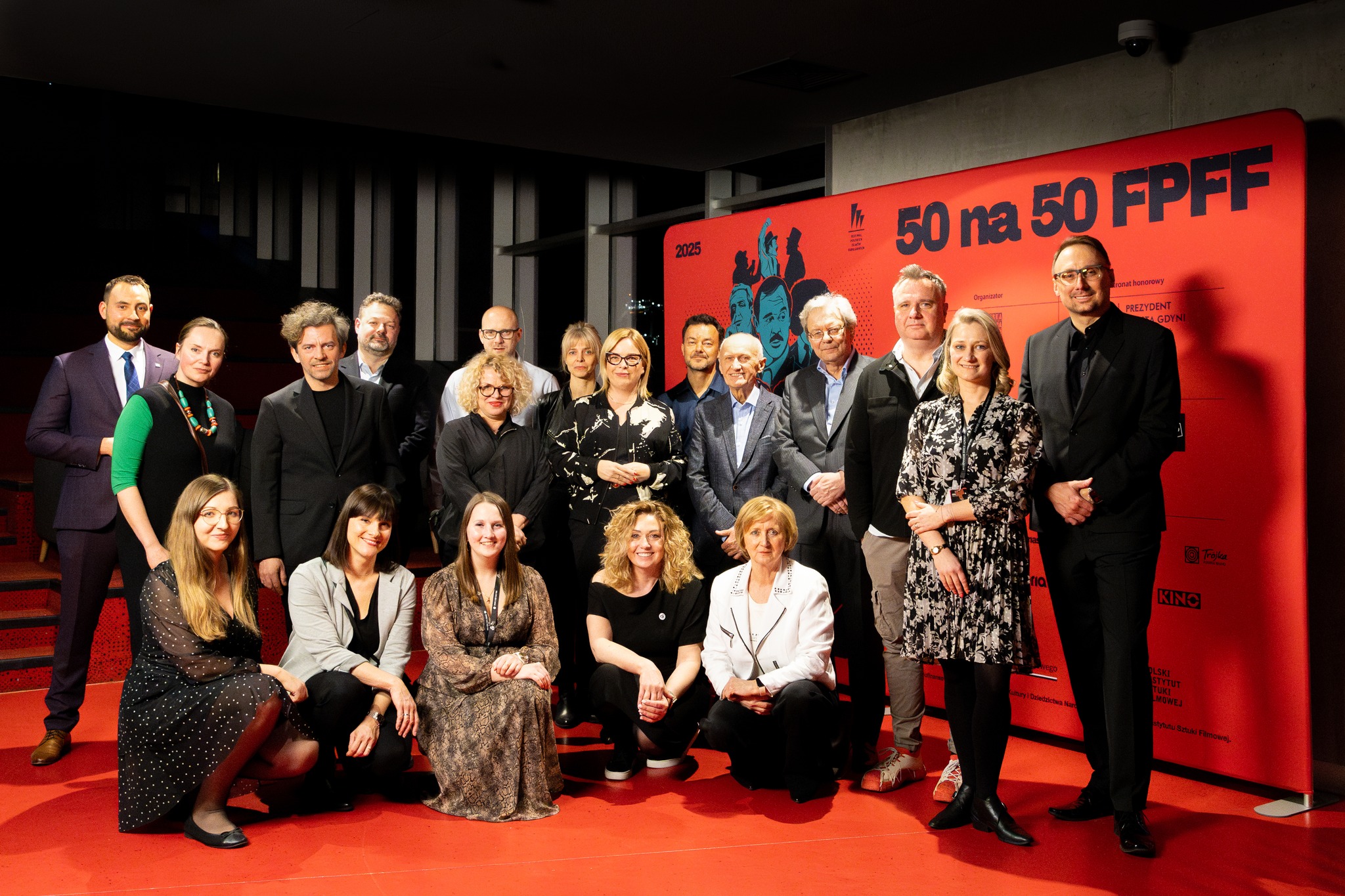 Zdjęcie grupowe po wydarzeniu w GCF-ie. Na ściance z napisem &bdquo;50 na 50&rdquo; stoją m.in.: wiceprezydentka Gdyni Oktawia Gorzeńska, dyrektorka artystyczna FPFF Joanna Łapińska, naczelnik Wydziału Kultury UMG Maja Wagner, dyrektor GCF Jerzy Rados