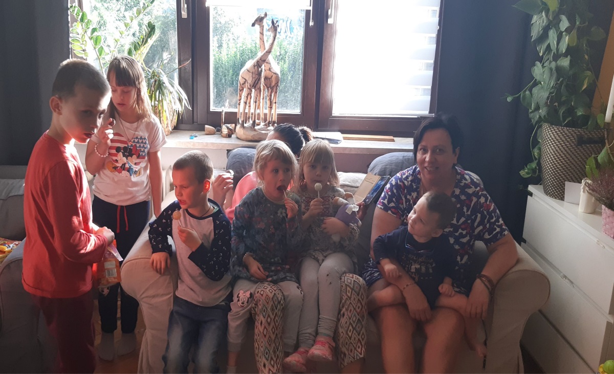 Zdjęcie przedstawia panią Maję Zadorożną siedzącą wraz z dziećmi na kanapie w salonie. 