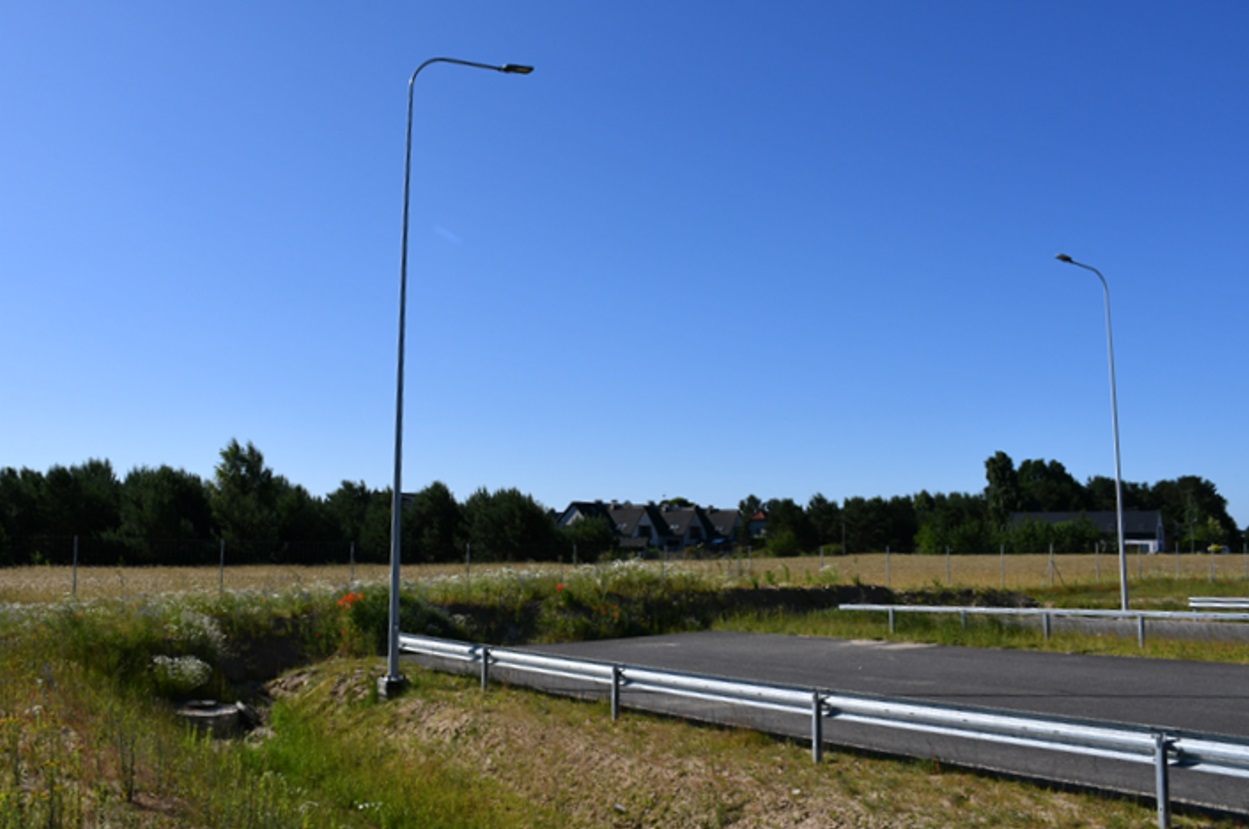 Droga, bariery, urwany przebieg, w tle łąka, r&oacute;w melioracyjny i zabudowania