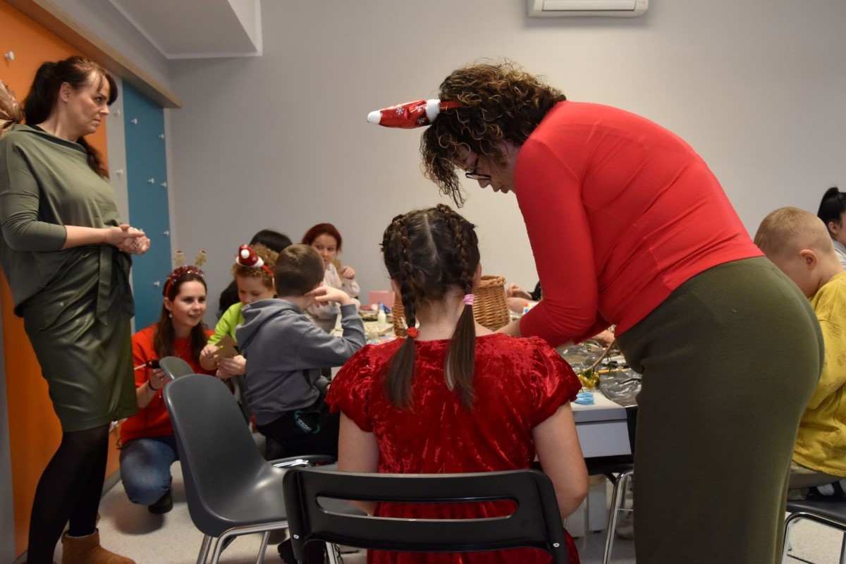 Na zdjęciu widzimy grupę ludzi w r&oacute;żnym wieku - dorosłych oraz ich dzieci. Pracują oni nad świątecznymi ozdobami podczas zorganizowanej przez DOPS 2 wigilii. 