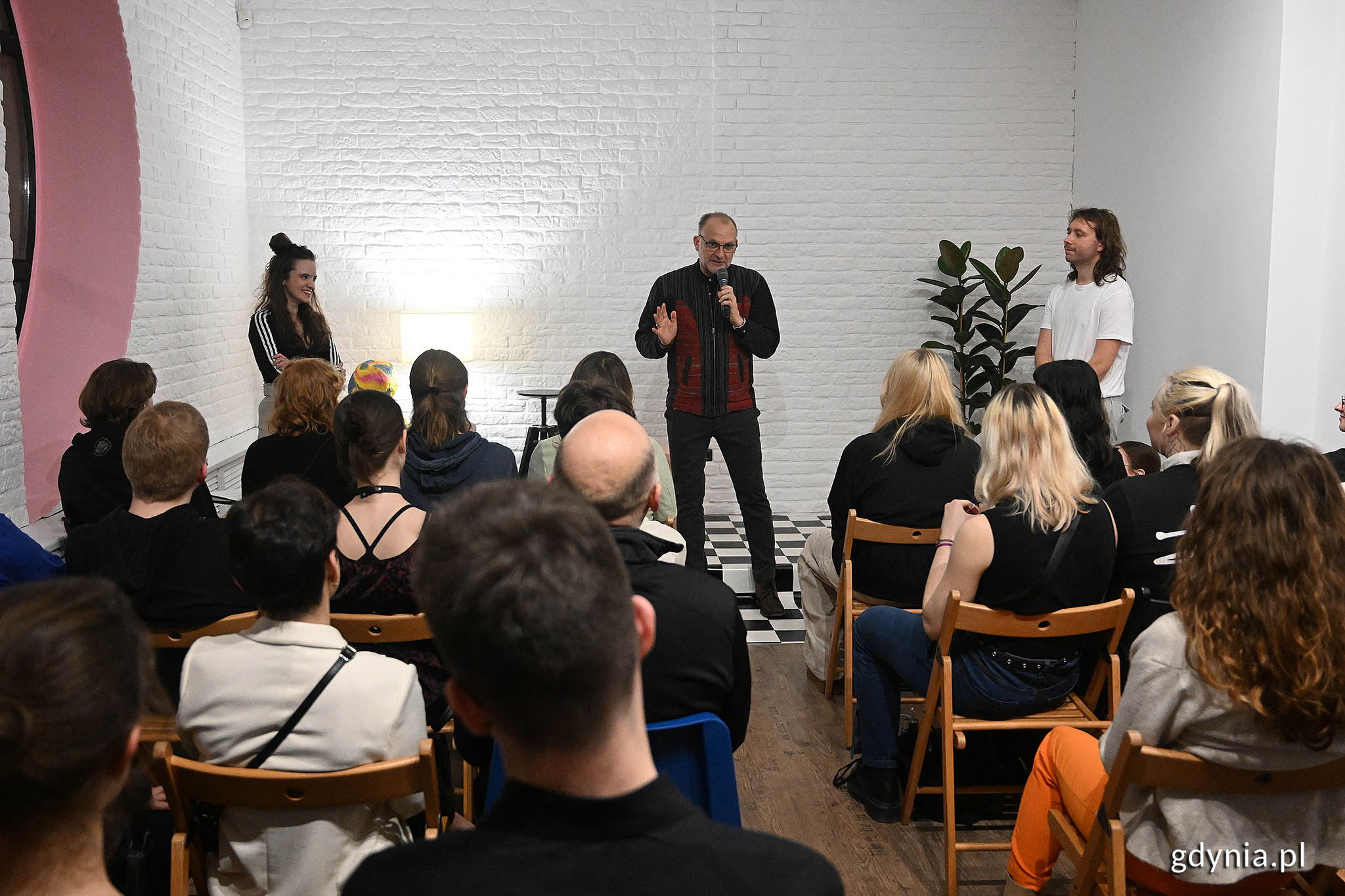 Mężczyzna z mikrofonem m&oacute;wi do grupy młodych ludzi zebranych w centrum sztuki.