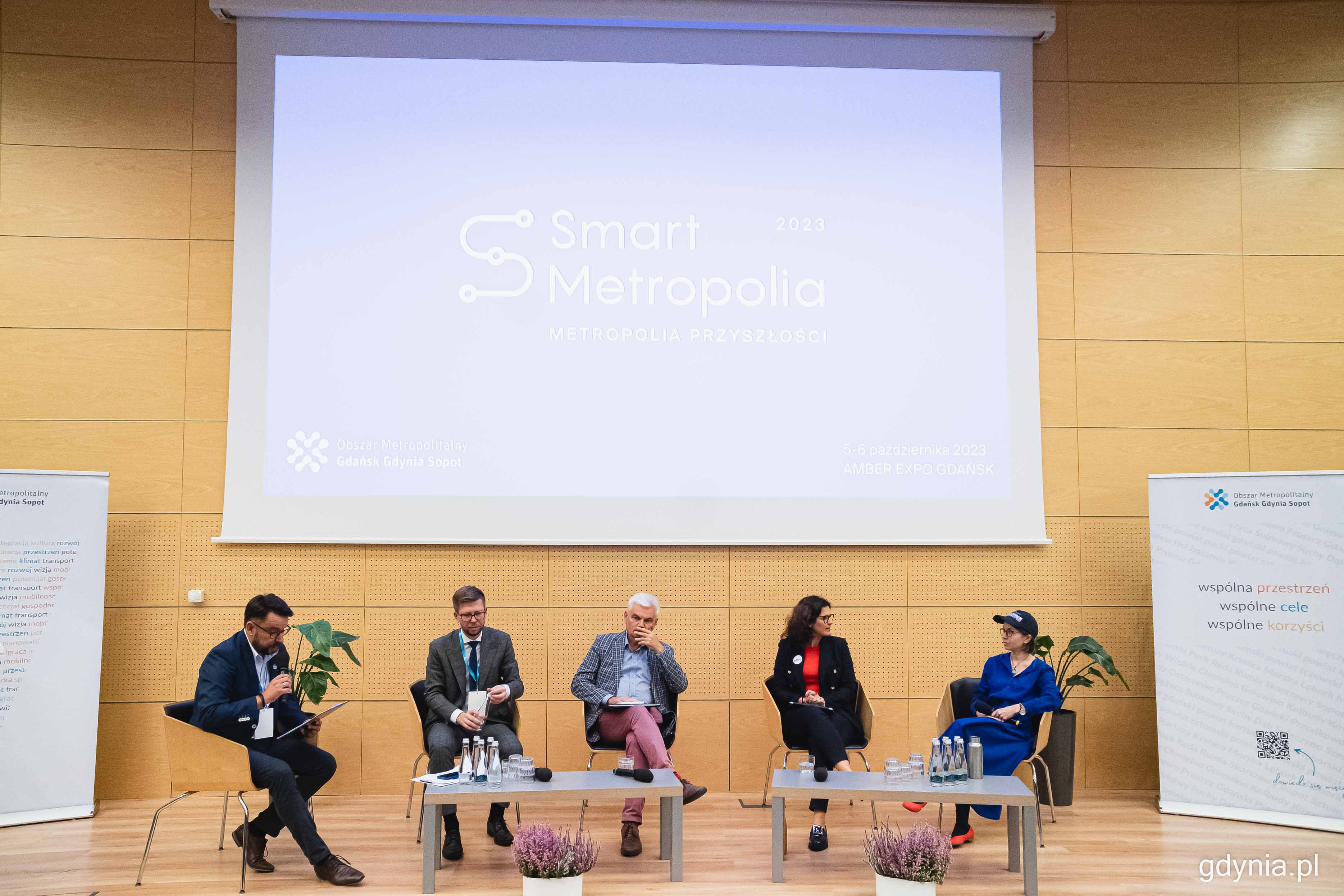 Sala konferencyjna, ekran z napisem Smart Metropolia, pięć os&oacute;b na scenie, siedzą w fotelach