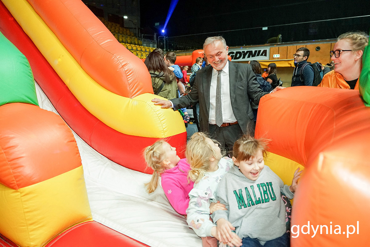 Mężczyzna, prezydent miasta, obserwuje dzieci zjeżdżające na dmuchanej zjeżdżalni.