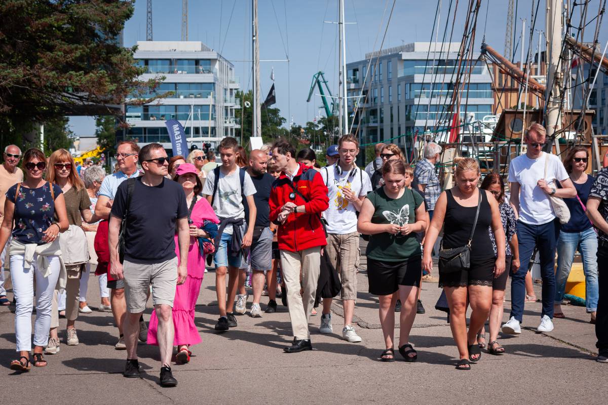 grupa os&oacute;b spacerująca wsp&oacute;lnie w Gdyni, w tle widoczne budynki i łodzie