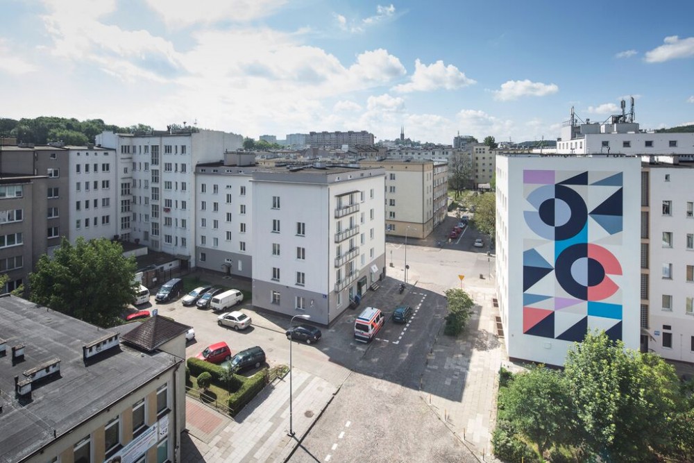Zdjęcie z g&oacute;ry na fragment ulicy Abrahama. Na ścianie bloku widoczny kolorowy, geometryczny mural