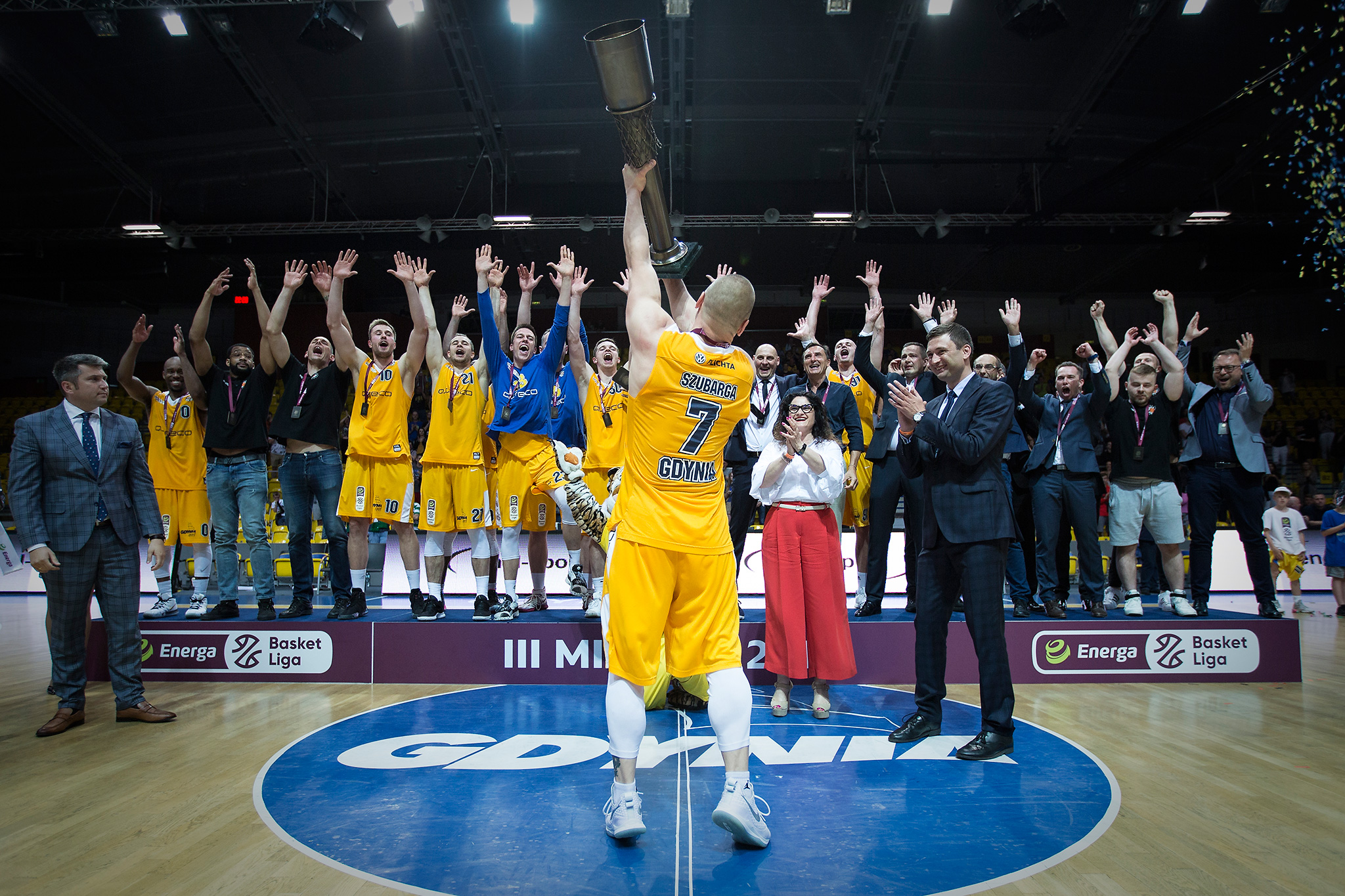 Na zdjęciu widzimy odwr&oacute;conego Krzysztofa Szubargę, kt&oacute;ry wznosi puchar za zdobycie brązowego medalu mistrzostw Polski, w tle drużyną Asseco Gdynia
