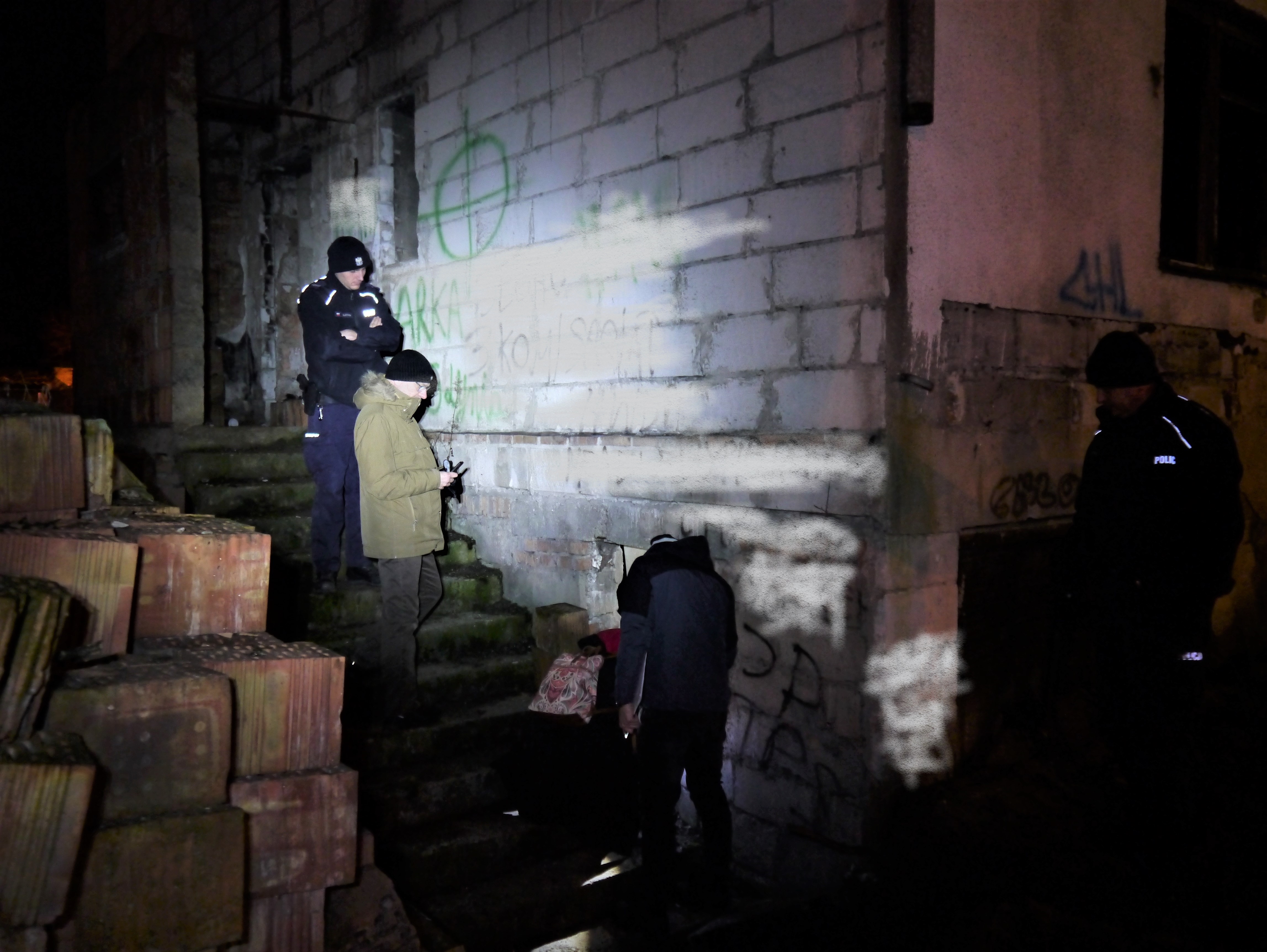 pracownicy stoją przed starym budynkiem i szukają bezdomnego