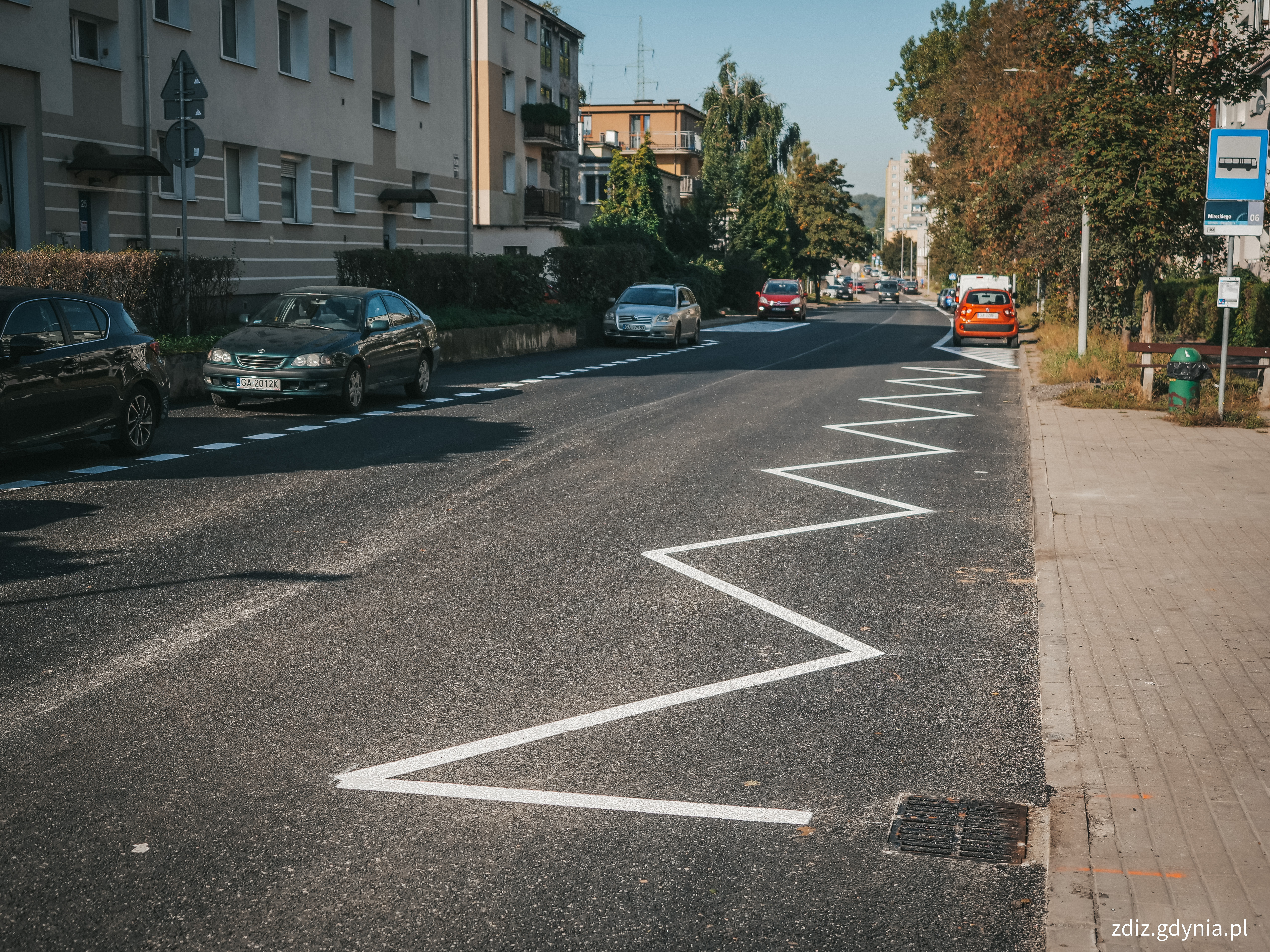 widok na ulicę z nową nawierzchnią i oznakowaniem, w tle budynki i zaparkowane pojazdy