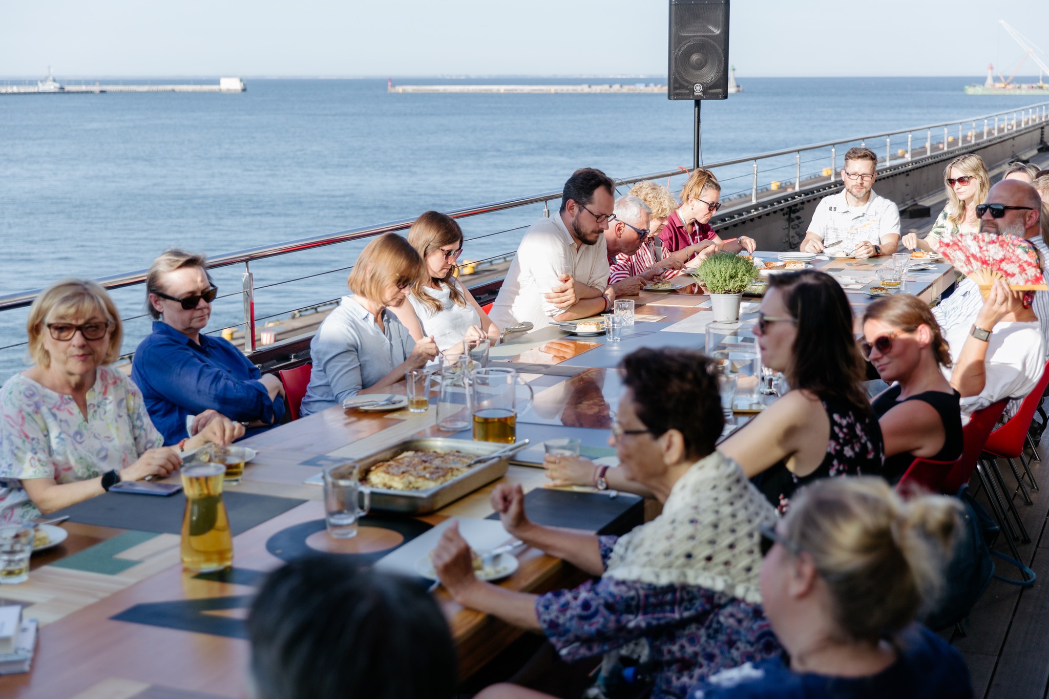 Ludzie przy wsp&oacute;lnym stole latem na tarasie Muzeum Emigracji