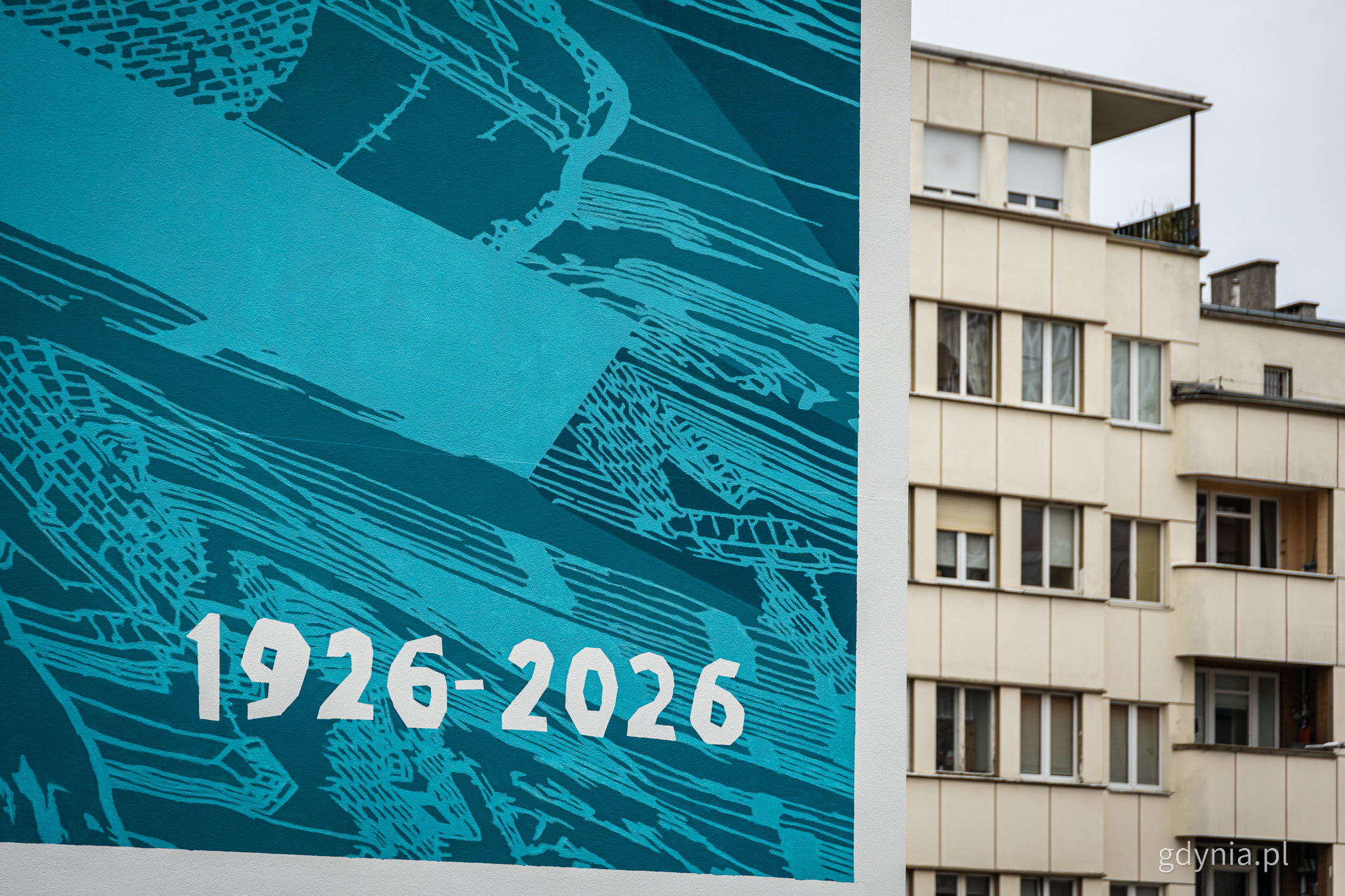 Widoczna elewacja modernistycznego budynku przy ul. Batorego, obok fragment jasnoniebieskiego muralu ściennego