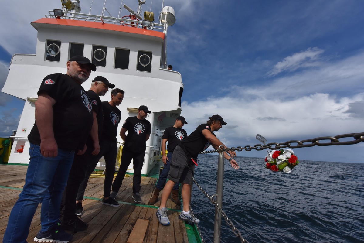 Członkowie 10. ekspedycji &bdquo;Santi. Odnaleźć Orła&rdquo; (od prawej): Tomasz Stachura, Karol Jacob, Michał Niemkiewicz, Maciej Honc, Piotr Michalik i Benedykt Hac stojący na pokładzie statku. Tomasz Stachura wrzuca do morza wiązankę biało-czerwonych kwiat&oacute;w ze wstążką z napisem "Chwała załodze ORP Orzeł" // fot. materiały &bdquo;Santi. Odnaleźć Orła&rdquo;