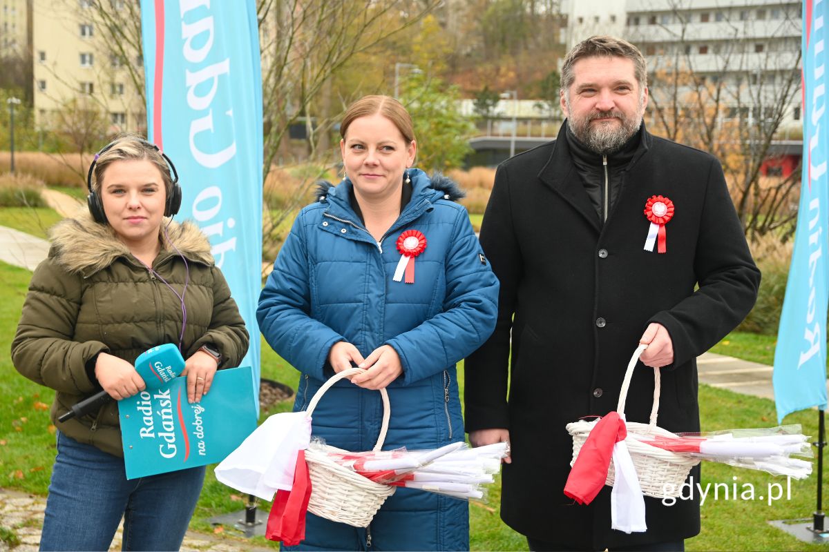 Dwie kobiety i mężczyzna stojący na placu z koszykami pełnymi polskich flag
