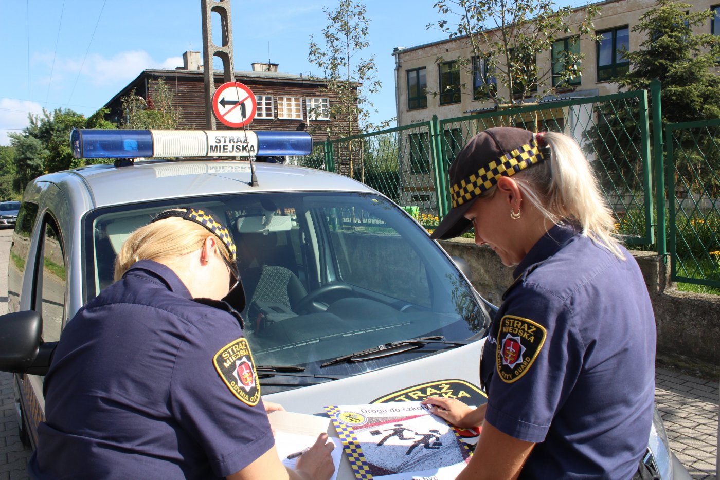 Radiow&oacute;z Straży Miejskiej, dwie strażniczki w mundurach, na masce rozłożone ulotki