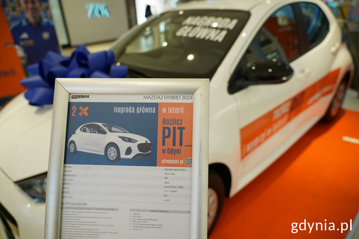 Hol Centrum Riviera, w tle samoch&oacute;d, Mazda 2 Hybrid, na pierwszym planie tabliczka z danymi technicznymi auta