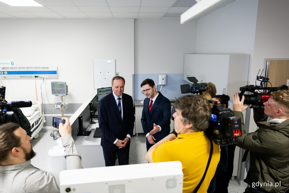 Mężczyzna oprowadza ludzi po oddziale szpitalnym, wok&oacute;ł dziennikarze z aparatami i kamerami.