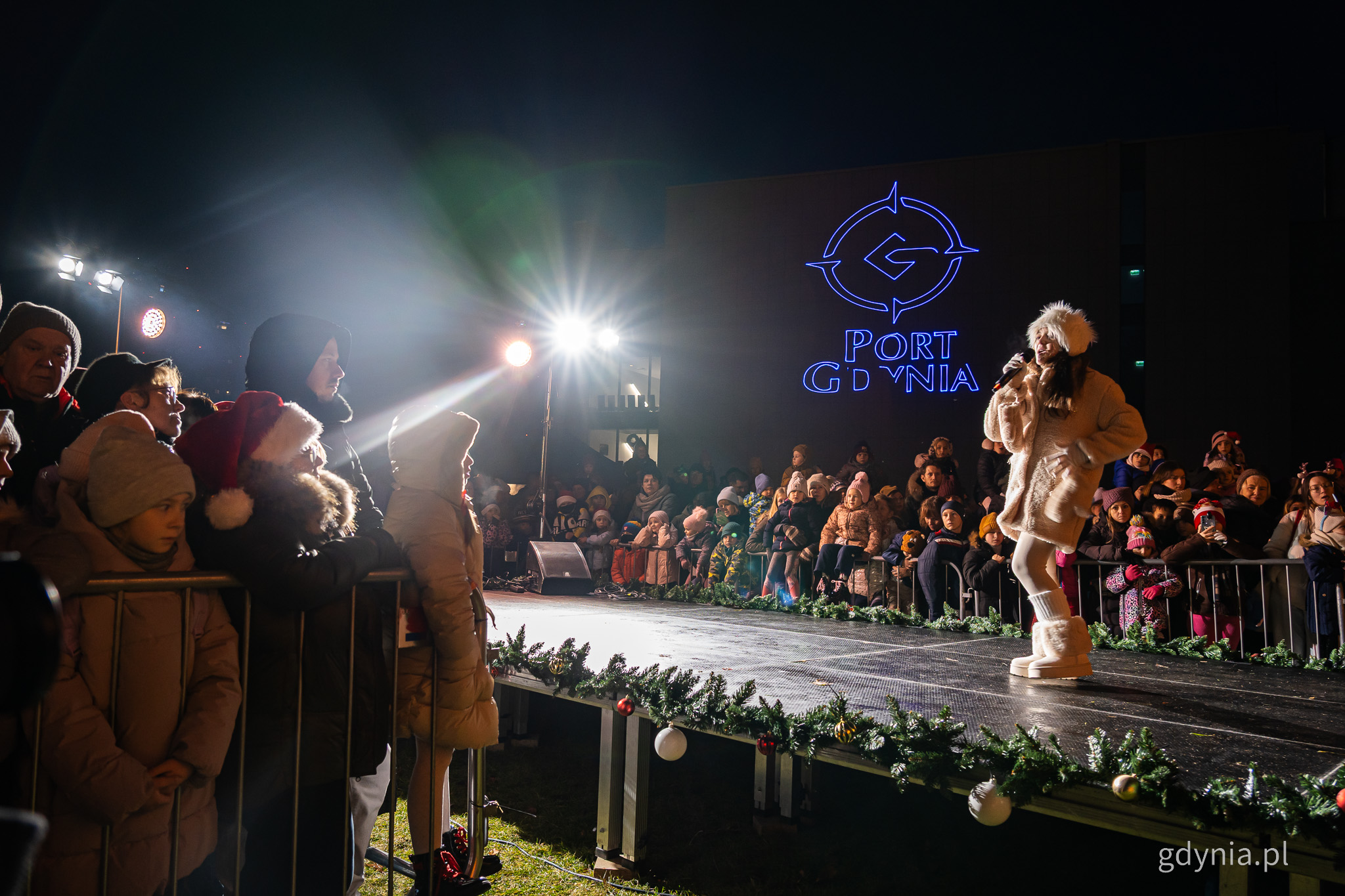 Scena plenerowa na placu Grunwaldzkim, wokalista śpiewa do mikrofonu, tłum widz&oacute;w, w tle na budynku logotyp Portu Gdynia