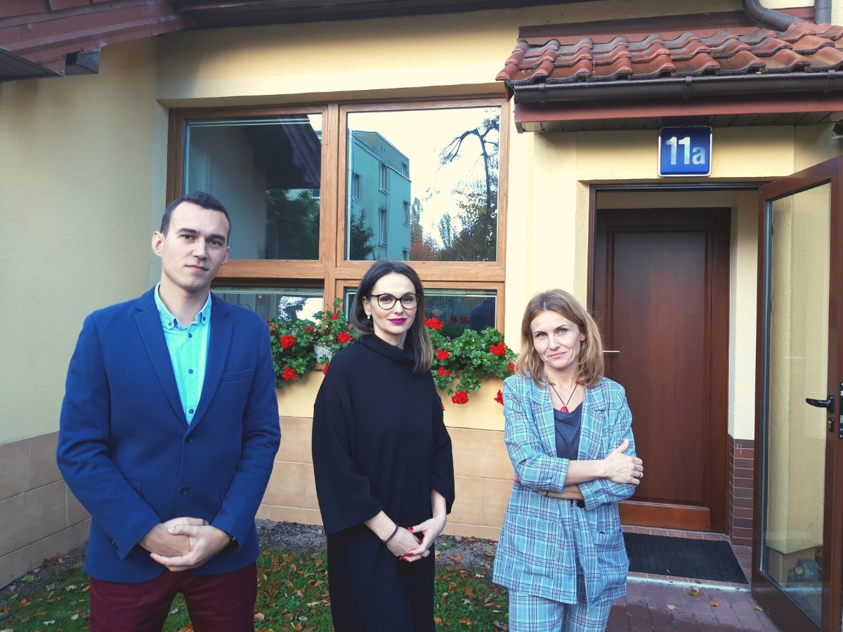 mężczyzna i dwie kobiety stoją przed ż&oacute;łtym budynkiem