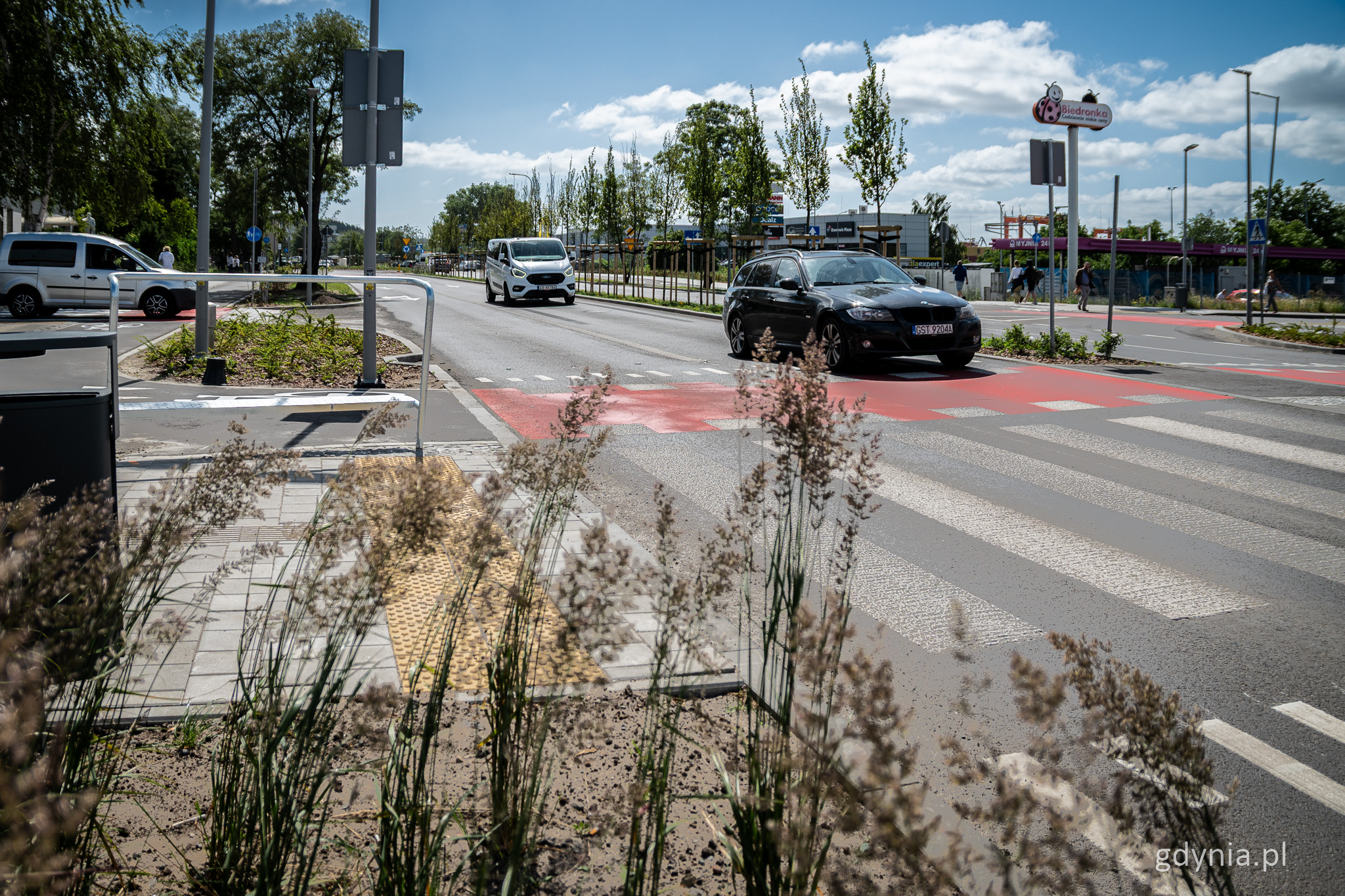 Ulica Unruga, dzień, jezdnia, przejście dla pieszych, zieleń przy drodze, czerwona droga rowerowa, kilka aut na jezdni