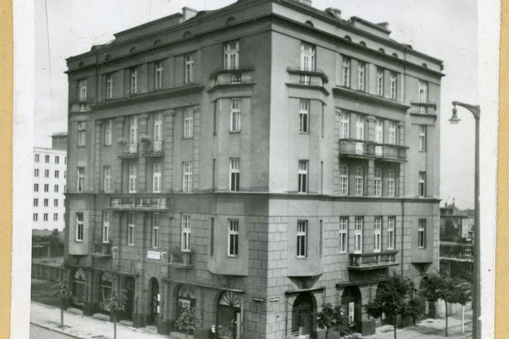 Zdjęcie archiwalne, czarnobiałe. Przedstawia kamienicę oraz fragmenty otaczającej ją ulicy i drzew. 