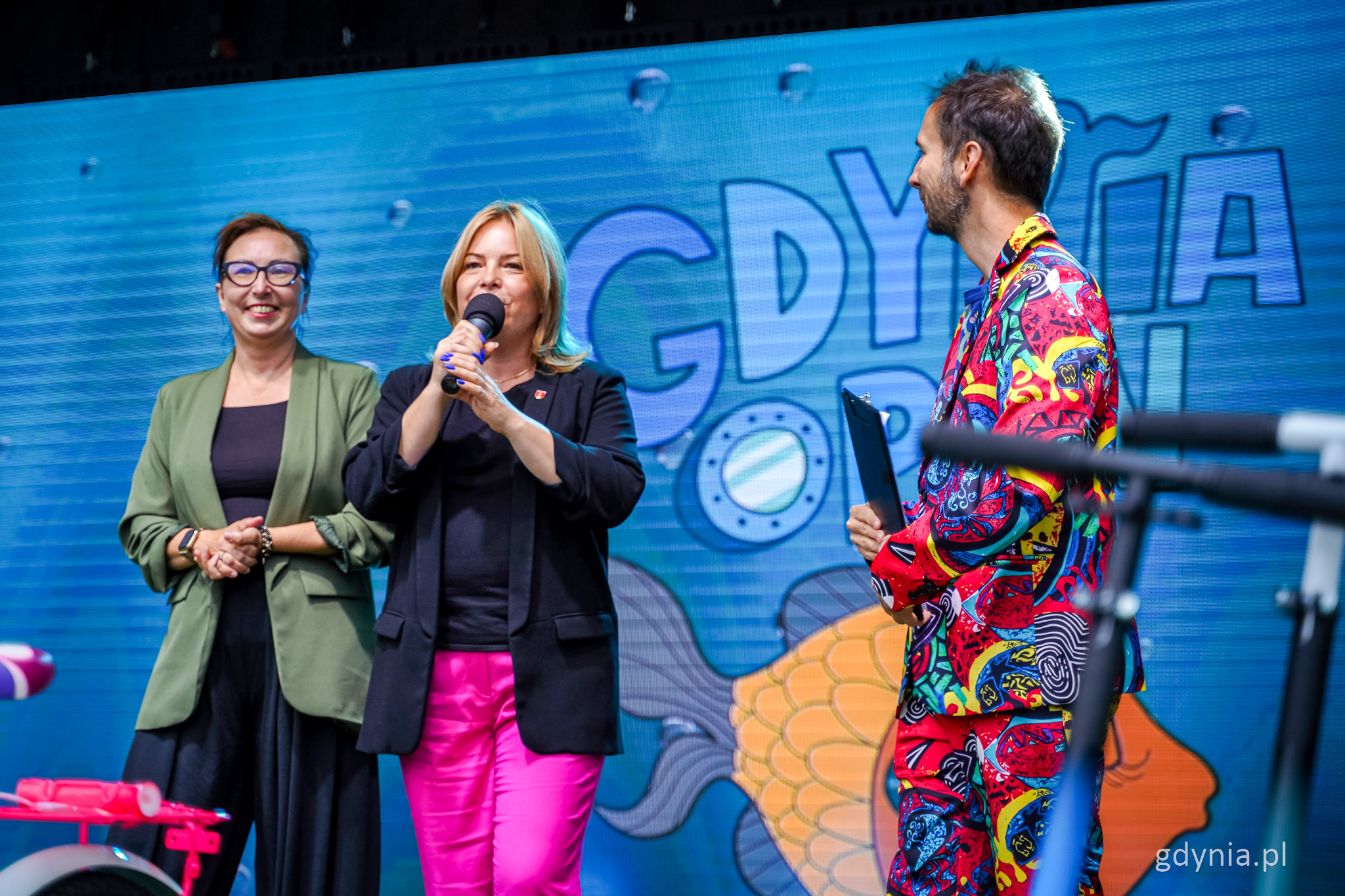 Scena w muszli koncertowej, w tle logo Gdynia Open, przemawia Oktawia Gorzeńska, obok Jolanta Jankowska-Żmich i Szymon Jachimek