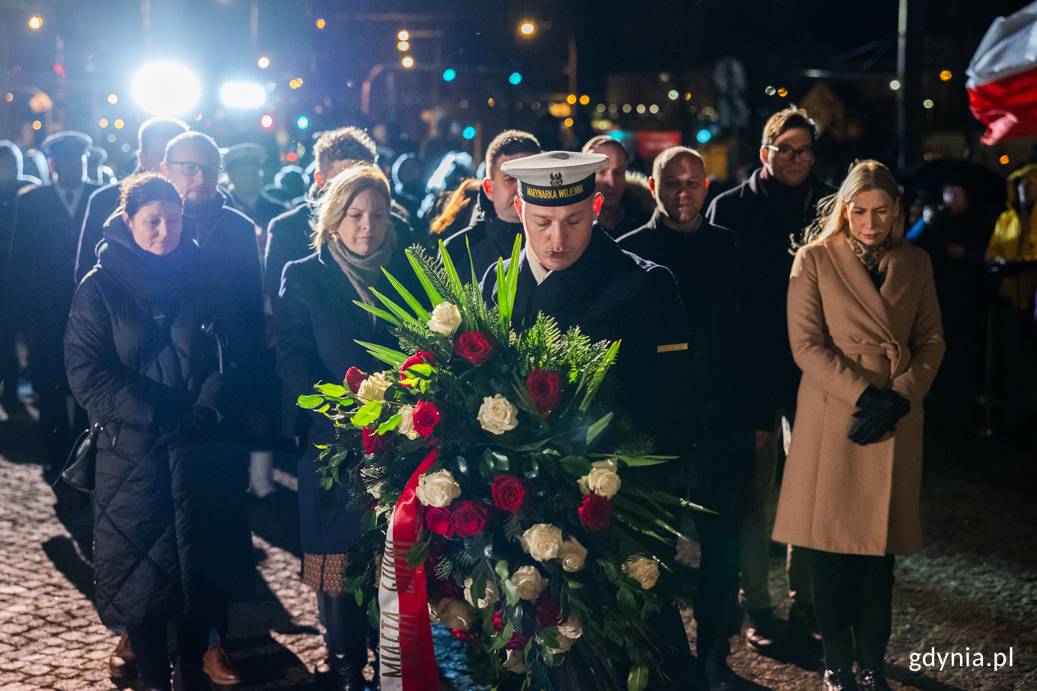 Żołnierz Marynarki Wojennej składa wieniec kwiat&oacute;w pod pomnikiem, za nim stoją przedstawiciele władz miasta