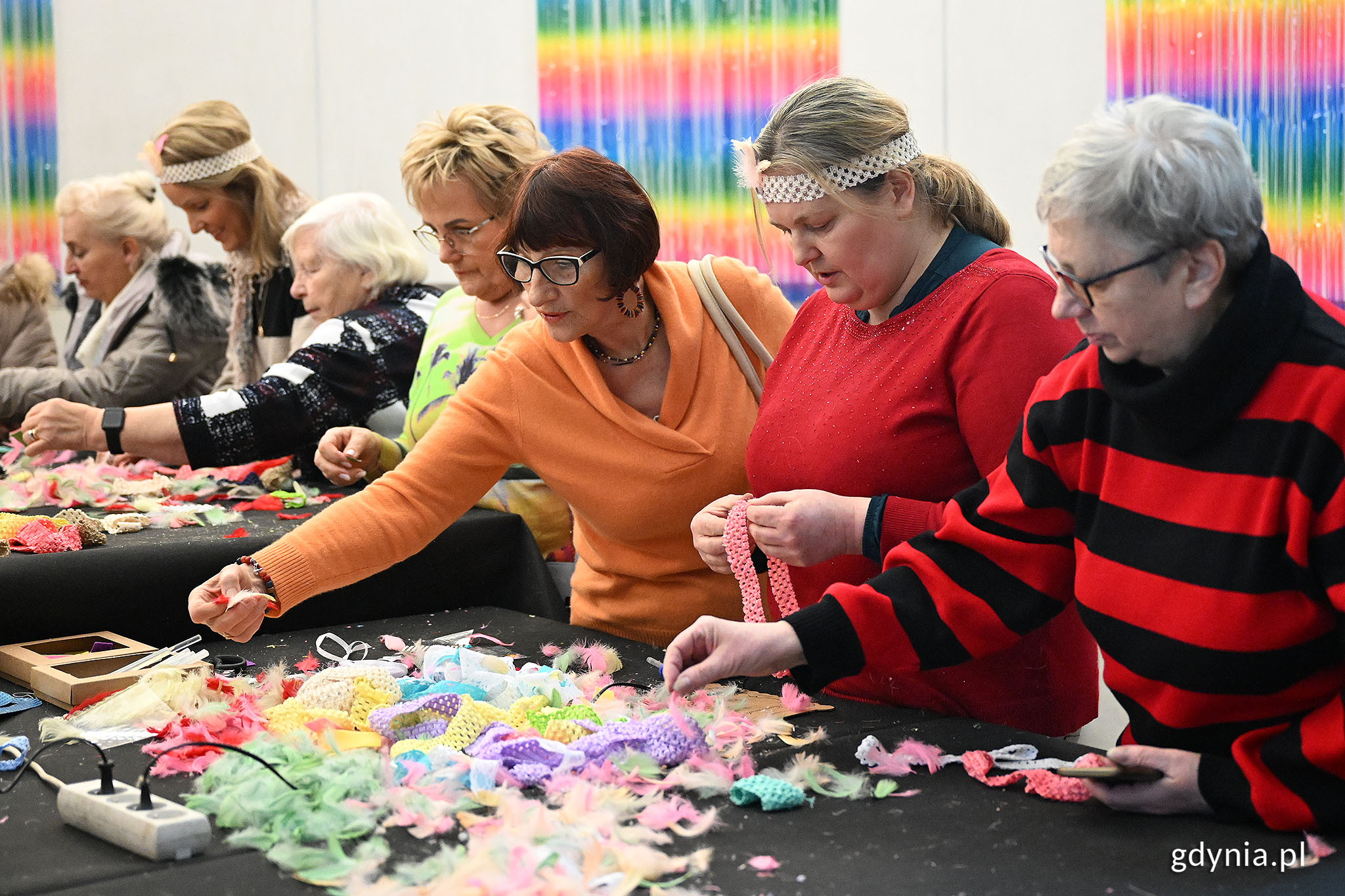 Grupa starszych os&oacute;b, kolorwe dekoracje na stole, osoby przeglądają dekoracje