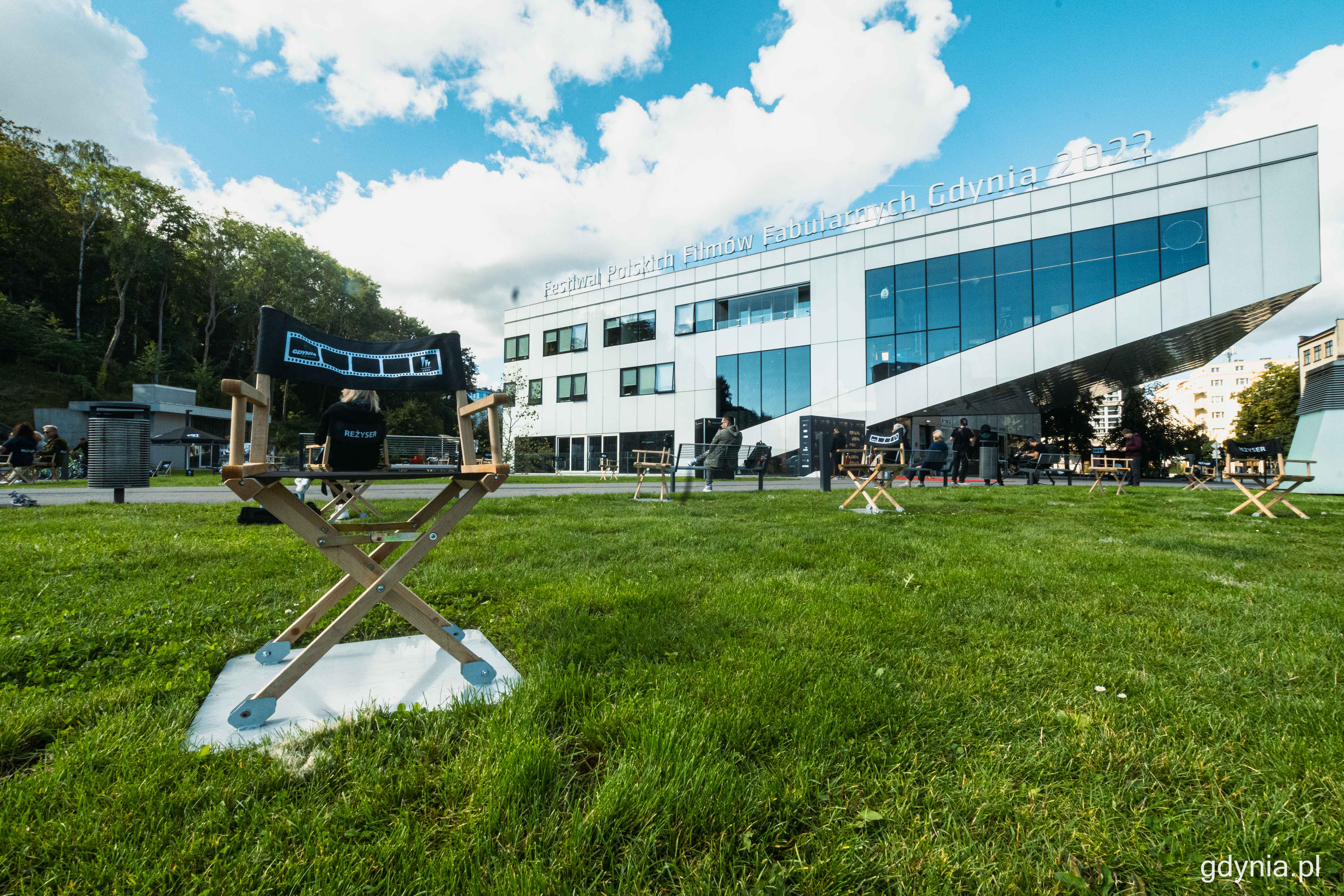 na zdjęciu fotel reżyserski stojący na trawniku, w tle biały budynek Gdyńskiego Centrum Filmowego z napisem 47. Festiwal Polskich film&oacute;w Fabularnych Gdynia 2022