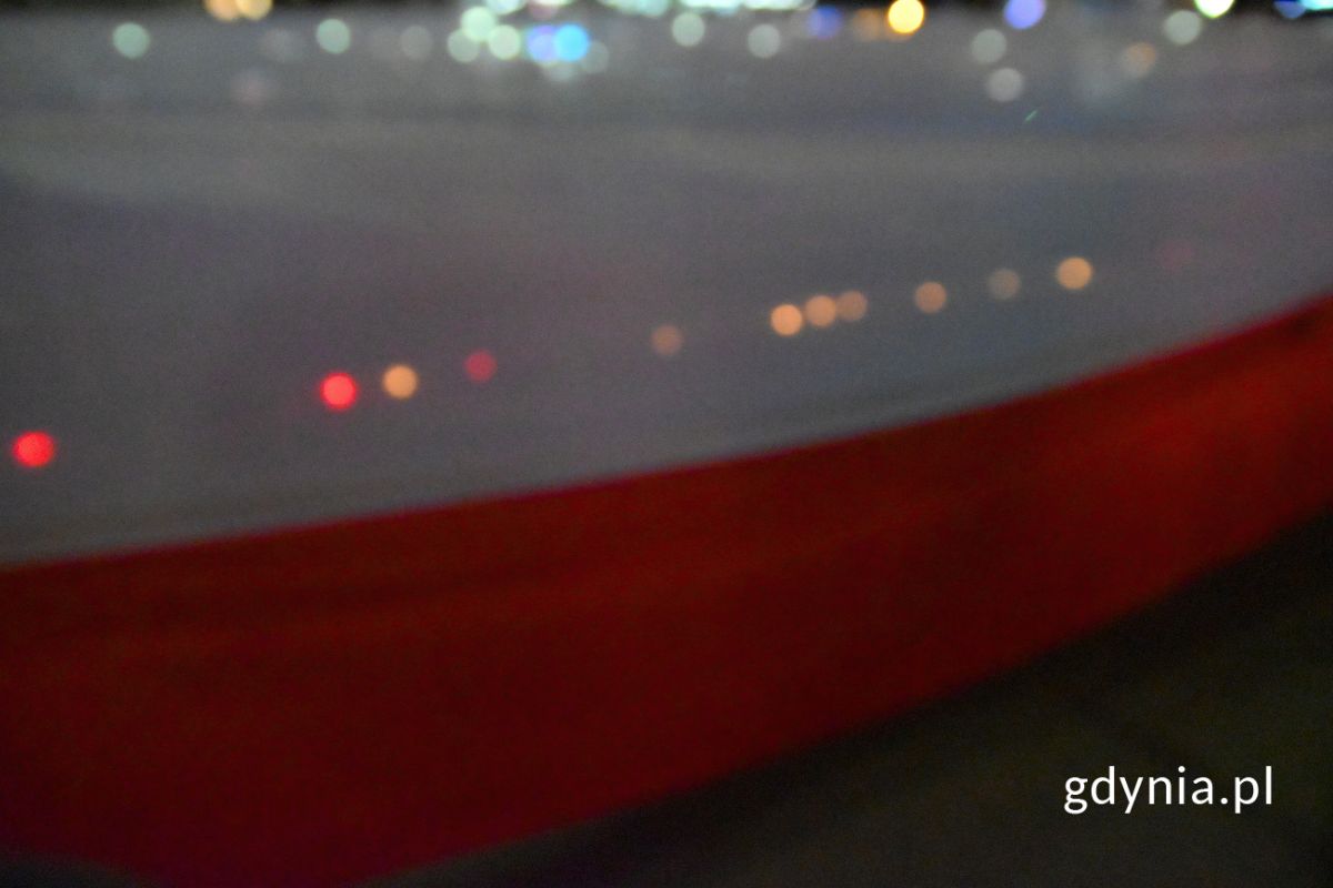 biało-czerwona flaga, przez kt&oacute;rą przebija się światło zniczy