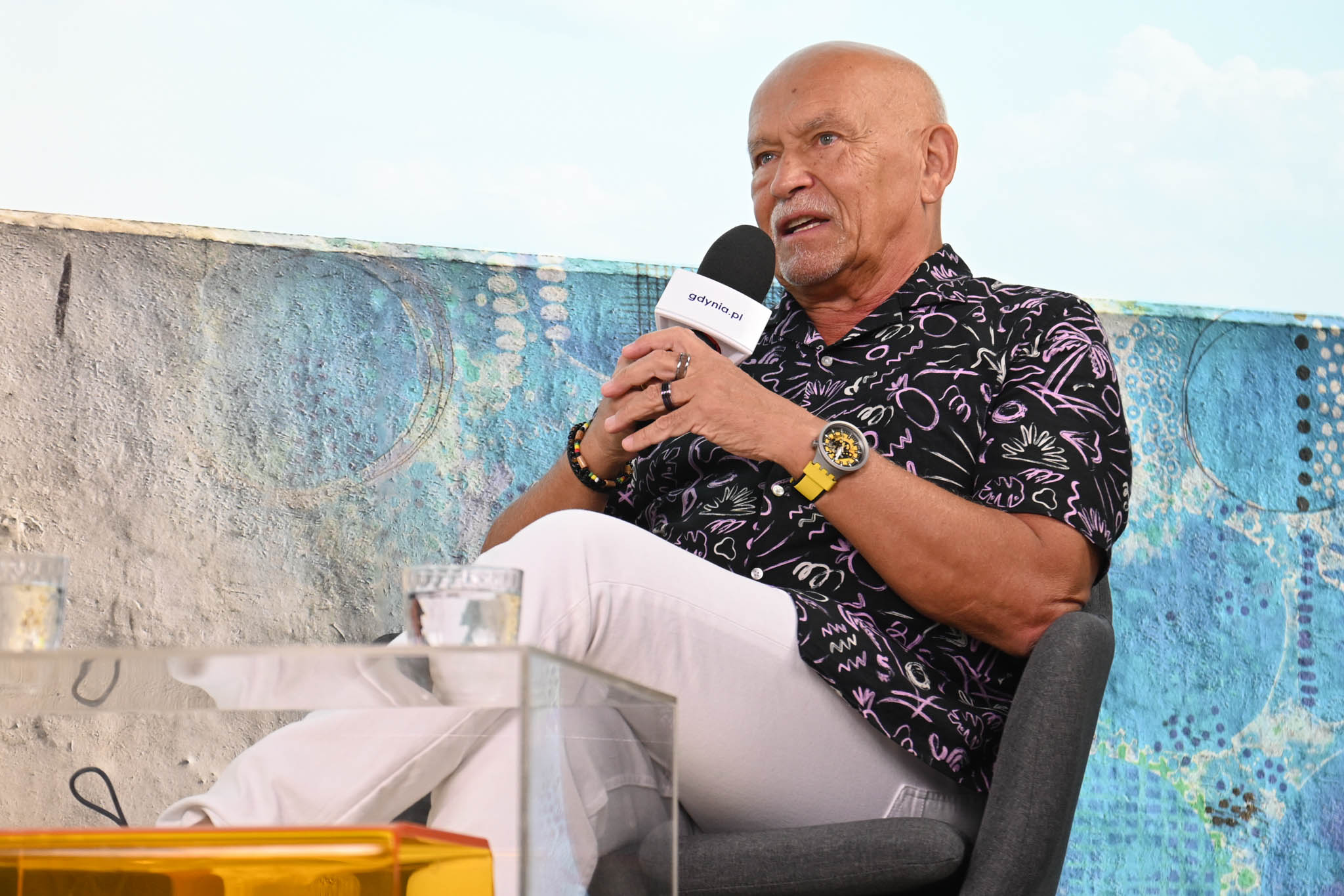 Andrzej Pągowski m&oacute;wi do mikrofonu, siedzi w fotelu, błękitne tło