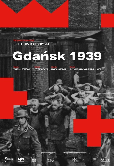 Plakat promocyjny filmu pt. "Gdańsk 1939". Czarno-białe zdjęcie na kt&oacute;rym widać niemieckiego żołnierza prowadzącego tłum ludzi z rękami założonymi na głowach. W tle ceglany budynek. O ścianę opiera się mężczyzna, kt&oacute;ry przygląda się prowadzonej kolumnie. U g&oacute;ry białe i czerwone napisy z nazwą filmu oraz informacjami o tw&oacute;rcach // fot. materiały prasowe