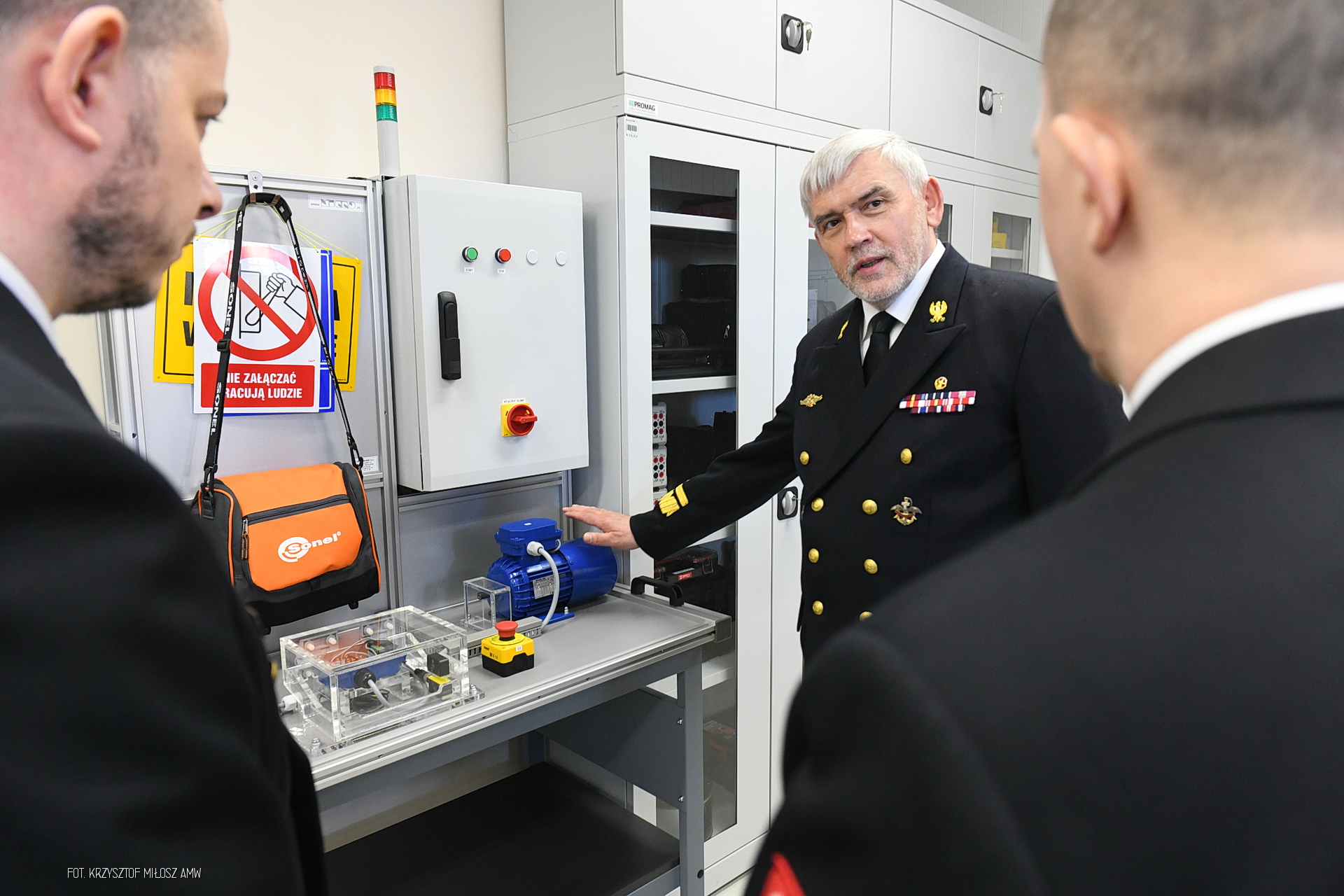 Wnętrze pracowni AMW, aparatura na stole, kilku mężczyzn rozmawia i wskazuje na urządzenia