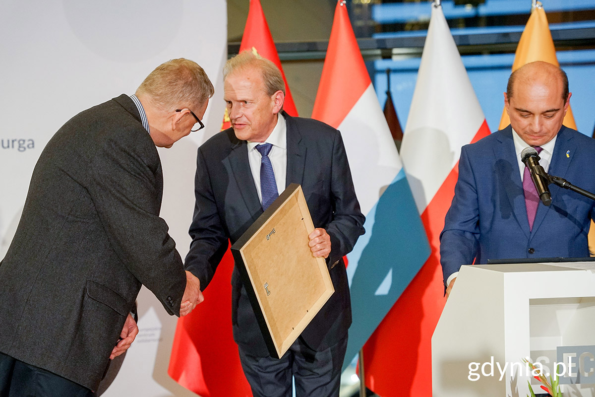 Mężczyzna wręcza nagrodę drugiemu mężczyźnie na scenie.