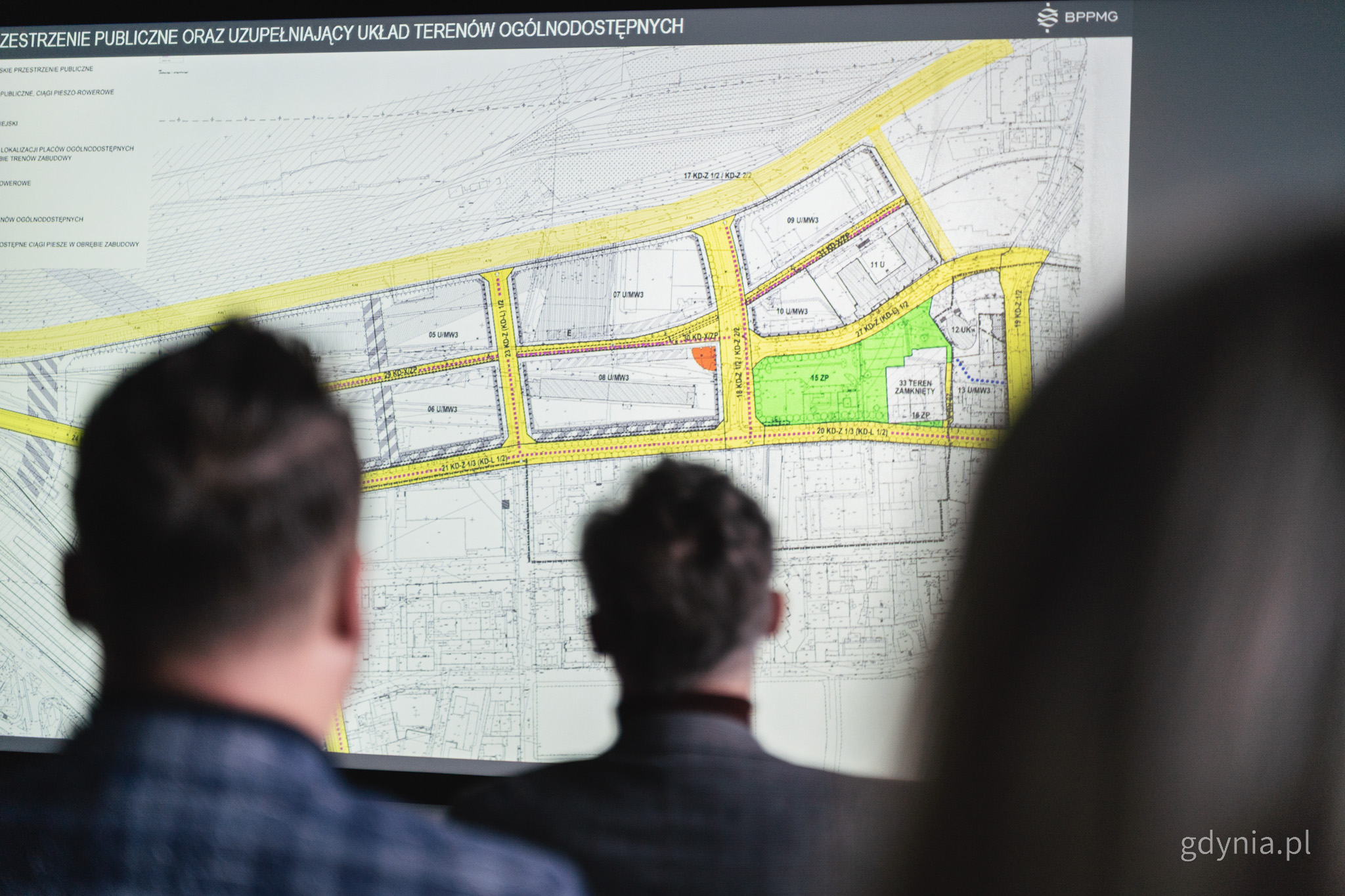 Sala konferencyjna, widocznych kilka os&oacute;b, ekran z wyświetlanym planem zagospodarowania