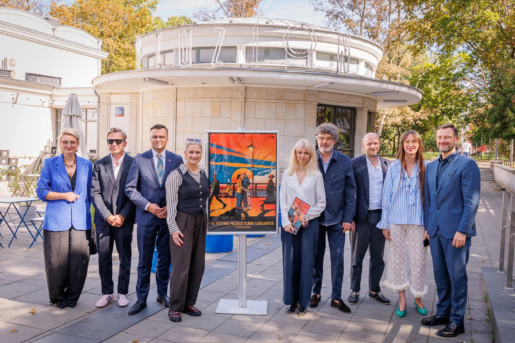 Plac przed Kinem Iluzjon w Warszawie, grupa os&oacute;b organizator&oacute;w FPFF pozuje do zdjęcia, miedzy nimi plakat festiwalu