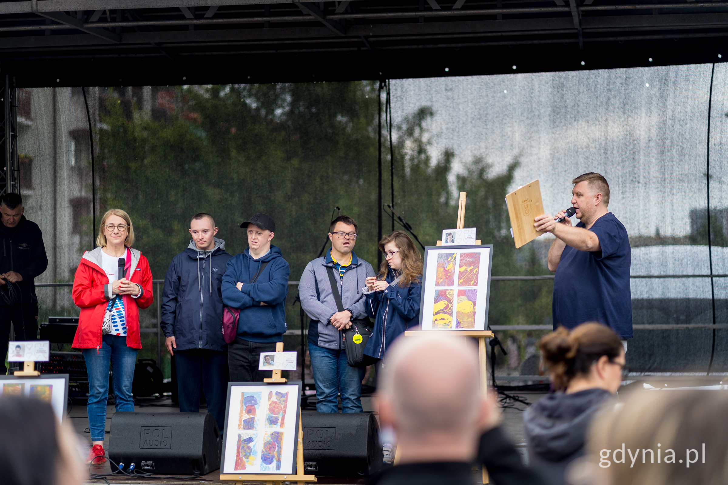 Scena, kilkoro dzieci, prowadzący - mężczyzna z mikrofonem, na scenie wystawione dwie sztalugi z pracami plastycznymi