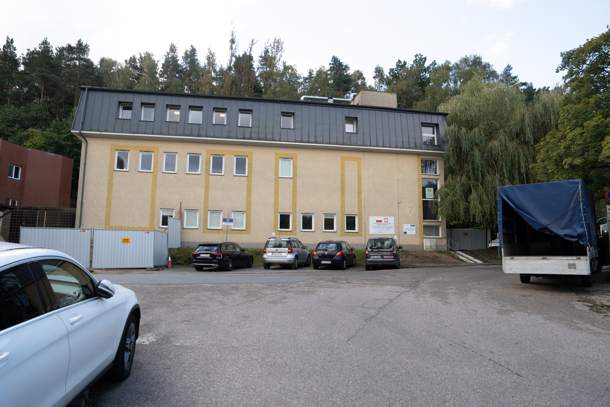 Teren Szpitala Morskiego, budynek z ż&oacute;łtą elewacją, parking z kostki brukowej, samochody