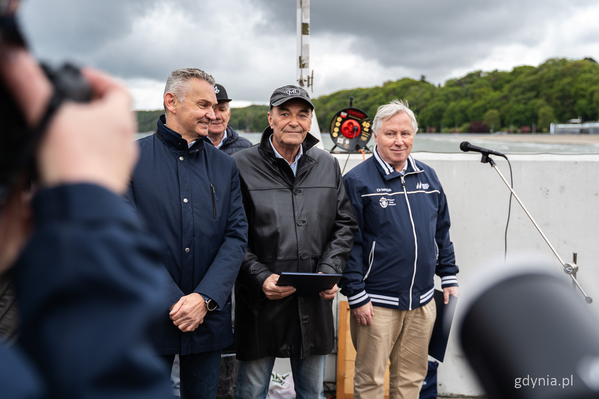 Falochron, marina w Gdyni, trzech mężczyzn pozuje do zdjęcia, ludzie dookoła, mikrofon na statywie