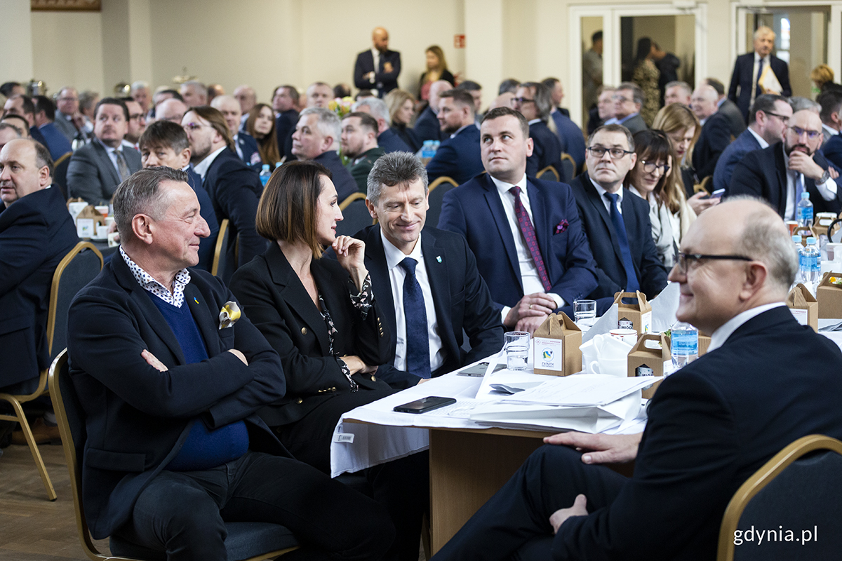 Ludzie zgromadzeni na sali siedzą za stołami.