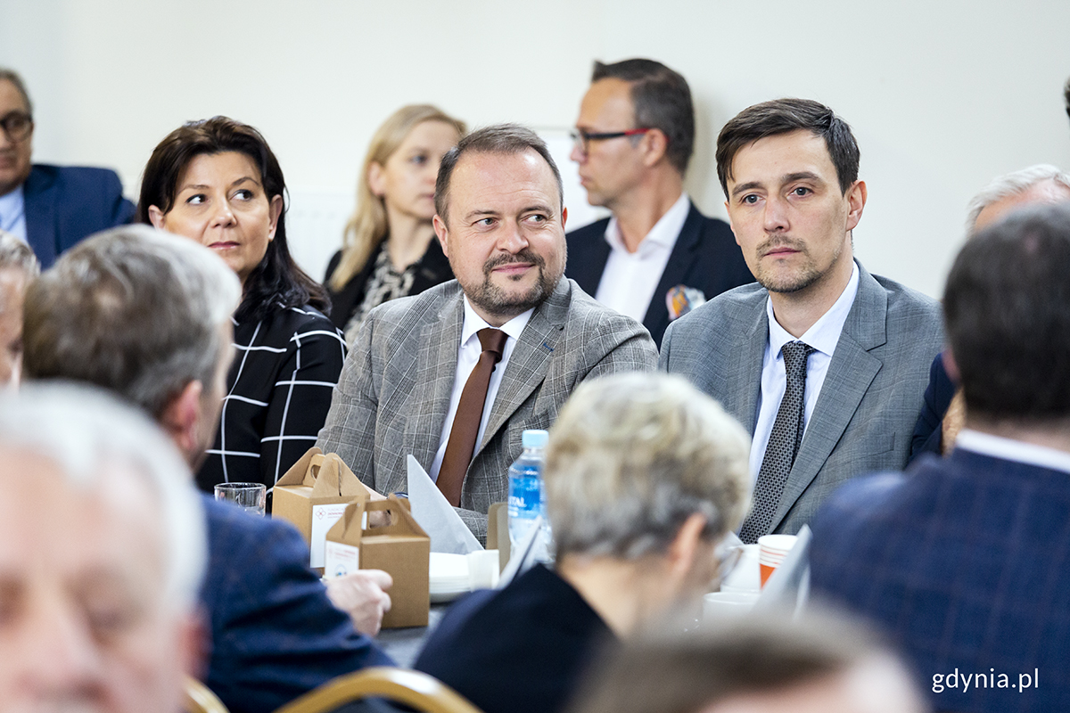 Ludzie zgromadzeni na sali siedzą za stołami.