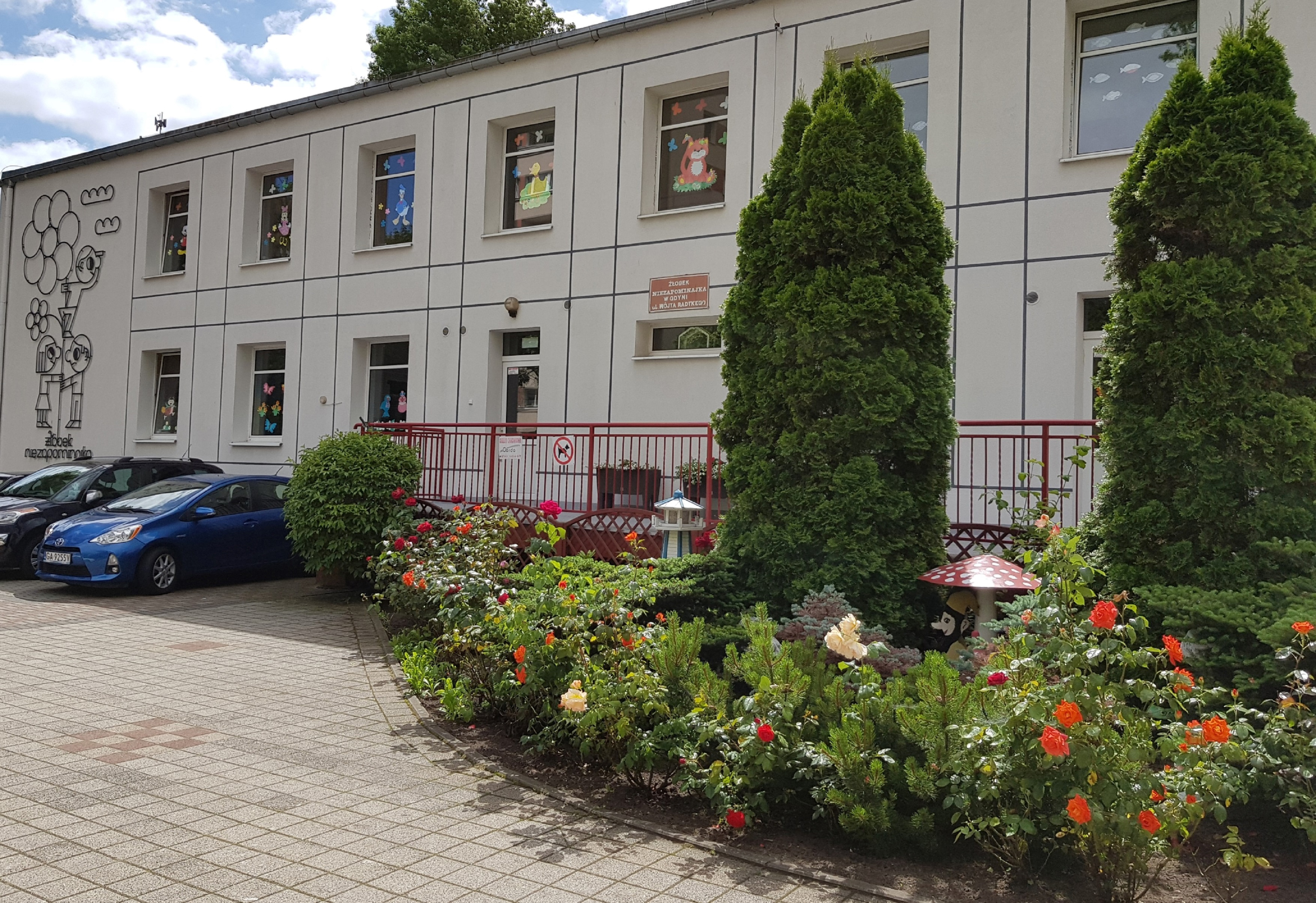 Ogr&oacute;d przy Żłobku "Niezapominajka", w kt&oacute;rym przeważają r&oacute;że, iglaki, bajkowe figurki i, co ciekawe, nie ma tam niezapominajek