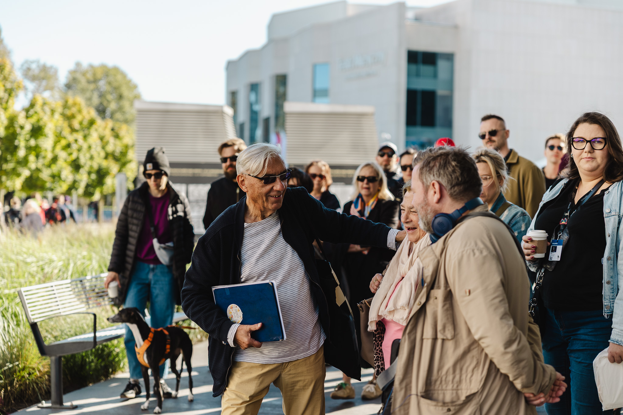 Grupa ludzi prowadzona przez przez przewodnika Arka Brzęczka, ubranego z jasną koszulkę i ciemną kurtkę. W tle znajdują się budynki Teatru Muzycznego i Gdyńskiego Centrum Filmowego 