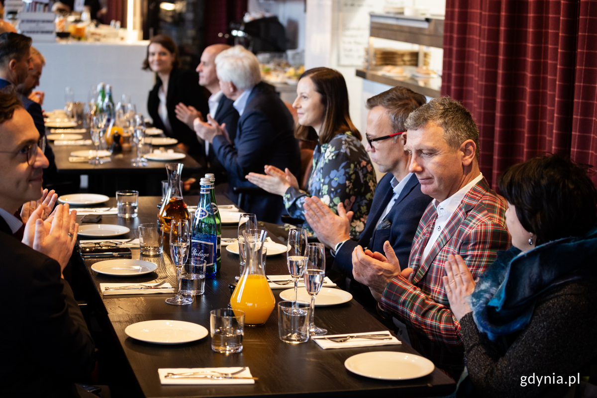 Ludzie siedzą przy stole w restauracji i bija brawo.
