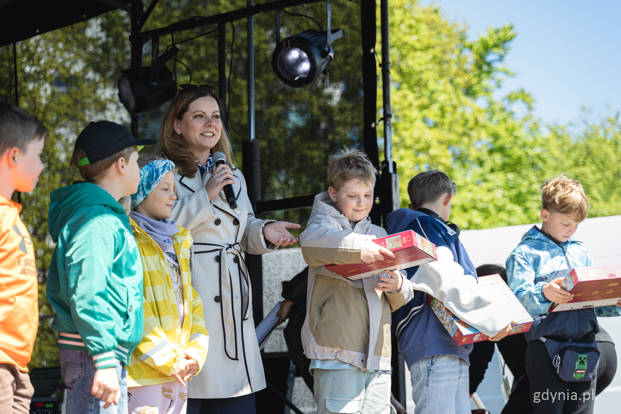 Scena plenerowa, kilkoro dzieci, w środku stoi i przemawia przez mikrofon Aleksandra Kosiorek