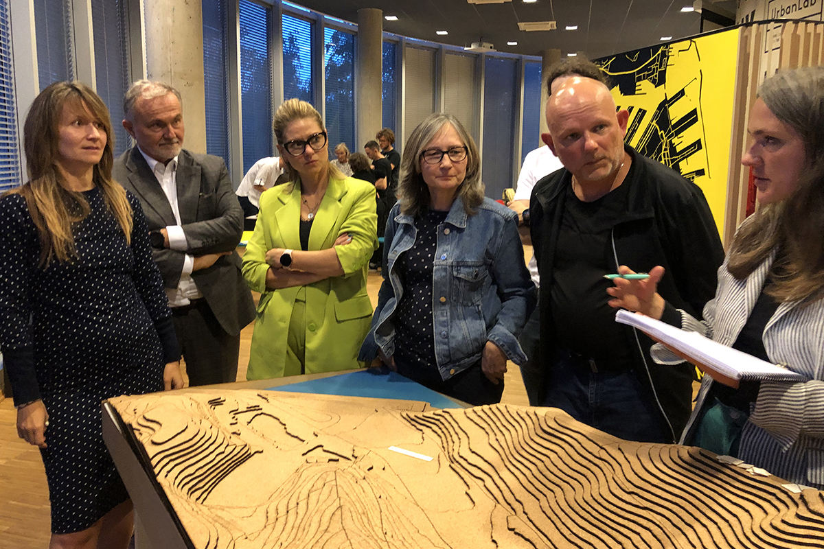 Kilka os&oacute;b rozmawia nad plastyczną mapą terenu na stole.