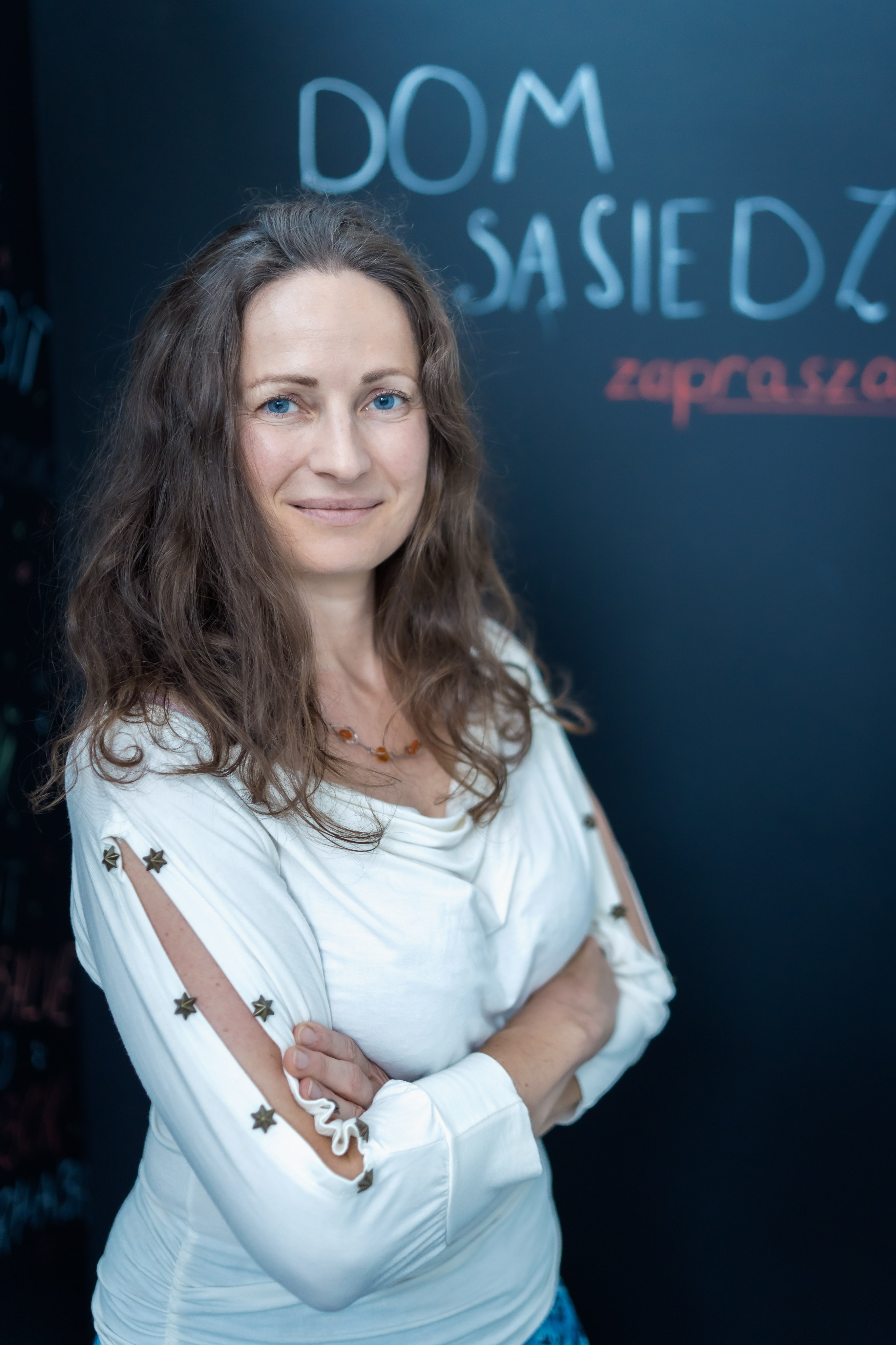 Przez kilka miesięcy po wybuchu wojny w Ukrainie Przystanie były schronieniem dla setek os&oacute;b uchodźczych, kt&oacute;re w Gdyni szukały bezpieczeństwa. I to właśnie jego zapewnienie było najważniejszym zadaniem, jakie stanęło przed animatorami dom&oacute;w sąsiedzkich, organizującymi codzienność w miejscach zbiorowego, tymczasowego pobytu. O tym, jak wyglądał tamten czas w Przystaniach, m&oacute;wią w dzisiejszej odsłonie cyklu &bdquo;Twarze Pomagania&rdquo;.   Ekipa &ldquo;Przystani&rdquo; i &ldquo;Wymiennikowni&rdquo; zapewniła osobom uchodźczym bezpieczeństwo w trudnych dniach po wybuchu wojny w Ukrainie // fot. Dawid Linkowski Początek roku 2022 upływał w Przystaniach na przygotowaniach do wznowienia działalności sąsiedzkiej po przerwie spowodowanej pandemią. Co więcej, na 1 marca zaplanowano otwarcie gruntownie przebudowanego budynku Przystani Chylońska 237 na Cisowej.  Ale nasilało się zagrożenie wybuchem wojny tuż za wschodnią granicą. Towarzyszyły temu przygotowania do przyjęcia w Polsce os&oacute;b uchodźczych, kt&oacute;rych &ndash; gdyby spełnił się czarny scenariusz &ndash; spodziewano się w naszym kraju. Przygotowania trwały także w Gdyni. Jednym z element&oacute;w było wskazanie miejsc, w kt&oacute;rych miałyby zostać zorganizowane miejsca zbiorowego, kr&oacute;tkoterminowego pobytu dla uciekających przed wojną. Taką funkcję miały pełnić m.in. centra sąsiedzkie Przystań.  &ndash; Znając realia zagranicznych ośrodk&oacute;w dla uchodźc&oacute;w pomyślałam, że Przystanie będą dobrym miejscem tymczasowego, kr&oacute;tkoterminowego pobytu: są w nich kuchnie, prysznice, pomieszczenia, kt&oacute;re można zaadaptować na sypialnie i w kt&oacute;rych można zapewnić więcej intymności, niż w dużych halach sportowych &ndash; m&oacute;wi dziś Dobrosława Korczyńska-Partyka, kierowniczka Działu Przestrzeni Społecznych w Laboratorium Innowacji Społecznych w Gdyni, kt&oacute;re koordynuje sieć Przystani. &ndash; Wiedziałam, że jak najszybciej musimy się przygotowywać, więc zaczęliśmy rozmawiać w zespole o tym, co trzeba zrobić. W czasie tych rozm&oacute;w poczułam, że nikt z nas nie chciał być wtedy w innym miejscu. Chcieliśmy działać. Było dla nas oczywiste, że musimy się zaangażować.   Dobrosława Korczyńska &ndash; Partyka // fot. Dawid Linkowski Jędrzej Sołtysiak, w&oacute;wczas animator Przystani Chylońska 237, przyznaje, że wiadomość o tym, że w Przystani zamieszkają osoby uchodźcze, trochę go przestraszyła.  &ndash; Jestem zadaniowcem, więc skupiłem się po prostu na wykonaniu zadań, kt&oacute;re otrzymałem &ndash; m&oacute;wi. &ndash; Trochę w tym pierwszym etapie musiałem wyłączyć emocje i po prostu działać. 24 lutego 2022 roku Rosja zaatakowała Ukrainę.  W Przystaniach zorganizowano przestrzenie tak, by mogły w nich bezpiecznie zamieszkać osoby uciekające z Ukrainy. Dowieziono i rozstawiono ł&oacute;żka, pojawiły się pralki, lod&oacute;wki i drobny sprzęt kuchenny. Dzięki m.in. mieszkańcom do Przystani trafiała pościel, ręczniki, środki czystości, artykuły higieniczne, żywność, w&oacute;zki dla dzieci, zabawki, kosmetyki, żywność. Wszystko, czego potrzeba było osobom, kt&oacute;re uciekały zostawiając za sobą dorobek całego życia. Przystanie musiały być przygotowane na przyjęcie uchodźc&oacute;w w każdej chwili. Wcześniej jednak animatorzy wsparli punkt zakwaterowania zorganizowany w szkole podstawowej na Obłużu.   Przystań Lipowa 15. Przygotowanie miejsc dla os&oacute;b uchodźczych // arch. LIS Jako pierwsza osoby uchodźcze przyjęła Przystań Lipowa 15 w Wielkim Kacku, a po niej Przystanie: Śmidowicza 49 na Oksywiu i Chylońska 237 w Cisowej.  &ndash; Przyjeżdżały osoby, z kt&oacute;rymi mocno empatyzowaliśmy, kt&oacute;re chcieliśmy wesprzeć, stworzyć dla nich jak najlepsze warunki i sprawić, by poczuły się bezpiecznie &ndash; wspomina Dobrosława Korczyńska-Partyka.  Tym samym, animatorzy dom&oacute;w sąsiedzkich stanęli przed ogromnym wyzwaniem.  &ndash; Pierwszy raz w życiu miałam takie bliskie doświadczenie wojny &ndash; zauważa Anna Matłosz, socjoterapeutka z Przystani Opata Hackiego 33. &ndash; Mogło się wydawać, że toczyła się gdzieś daleko, ale działa się też u nas. W naszym miejscu pracy.   Anna Matłosz // fot. Dawid Linkowski Magdalena Janik pracowała w&oacute;wczas w Przystani Śmidowicza 49.  &ndash; Pamiętam przyjazd pierwszej grupy. Czekaliśmy cały dzień, autokar podjechał wieczorem. Wysiadły z niego osoby zmęczone, zagubione. Niekt&oacute;re z nich miały kilka walizek, niekt&oacute;re tylko jeden plecaczek. &ndash; Wspomina. &ndash; Wszystko było gotowe na ich przyjęcie, bo już wcześniej przygotowaliśmy kuchnię, łazienki i miejsca do spania: na sali gimnastycznej i w pokojach, w kt&oacute;rych były bardziej komfortowe warunki dla małych dzieci. Zadbaliśmy, by każdy znalazł na ł&oacute;żku podstawowe rzeczy: szczoteczkę i pastę do zęb&oacute;w czy ręcznik, a we wsp&oacute;lnej kuchni produkty, z kt&oacute;rych można przygotować posiłek.   Magdalena Janik // fot. Dawid Linkowski W pierwszych tygodniach animatorzy pełnili w Przystaniach kilkunastogodzinne dyżury &ndash; także w nocy. O tym czasie m&oacute;wią kr&oacute;tko: bardzo trudny i psychicznie, i fizycznie. Nikt nie był przygotowany na skalę spraw, z kt&oacute;rymi się mierzyli, bo nie było systemu, kt&oacute;ry w jakikolwiek spos&oacute;b regulowałby postępowanie w sytuacji, kt&oacute;ra właśnie się działa. Były łzy, poczucie bezsilności, czasami strach.  &ndash; Pierwsze dwa tygodnie to była praca siedem dni w tygodniu, z telefonem w ręku, z kr&oacute;tką przerwą na sen &ndash; opowiada Sviatlana Rasliakova, w&oacute;wczas w Przystani Śmidowicza 49. &ndash; Trzeba było wszystko zorganizować, znaleźć tłumaczy, wolontariuszy. Było dużo pytań, na kt&oacute;re nie było odpowiedzi, więc musieliśmy dzwonić, dzwonić, dzwonić. Nikt z nas nie miał doświadczenia w pracy interwencyjnej, w traumie, ale każdy z nas pracował najlepiej jak m&oacute;gł, potrafił i czuł. Dla mnie &ndash; Białorusinki mieszkającej od 11 lat w Polsce &ndash; było to wyzwanie na innym poziomie. Wszystko było mi bliższe, bardziej to przeżywałam. Rozmawiałam po rosyjsku, o czym zawsze uprzedzałam i co nie stanowiło problemu. Gdy wchodziłam do pracy, czekała na mnie kolejka os&oacute;b z mn&oacute;stwem pytań. W zaufaniu zwracano się do mnie, byłam &bdquo;swoja&rdquo;. I dobrze, i źle, bo gdzieś zacierała się granica. Przyjmowałam na siebie dużo trudnych historii. A że z wykształcenia jestem psychologiem, przeżywałam je bardziej.   Sviatlana Rasliakova // fot. Dawid Linkowski Renata Dębska pracowała w Przystaniach: Śmidowicza 49 i Chylońska 237. W obu przygotowano miejsca dla ponad 100 os&oacute;b. Gdy wszystkie były zajęte, pracy był ogrom: od zmiany pościeli, przez zamawianie posiłk&oacute;w, po umawianie wizyt u lekarzy specjalist&oacute;w, bo wiele os&oacute;b potrzebowało np. wsparcia psychologicznego.  &ndash; Wspieraliśmy w załatwianiu formalności urzędowych, pomagaliśmy zapisać dzieci do szk&oacute;ł czy przedszkoli, podpowiadaliśmy, jak szukać pracy &ndash; wylicza. &ndash; Wydawaliśmy leki, kosmetyki czy ubrania. Prowadziliśmy zbi&oacute;rki niezbędnych rzeczy, kt&oacute;rych w danym momencie brakowało.  Animatorzy m&oacute;wią, że ich praca była możliwa dzięki wsp&oacute;łpracy z Urzędem Miasta Gdyni i innymi jednostkami miejskimi, ale przede wszystkim: dzięki ogromnemu zaangażowaniu mieszkańc&oacute;w. Od pierwszych dni po wybuchu wojny gdynianki i gdynianie dostarczali dary, byli wsparciem w każdej sytuacji, kt&oacute;ra tego wymagała. Drzwi Przystani praktycznie się nie zamykały za osobami, kt&oacute;re chciały pom&oacute;c. Pytały, czego potrzeba &ndash; i natychmiast to organizowały. Od zabawek, przez odciągacze do pokarmu po transport do nowego miejsca zamieszkania. To wielkie sąsiedzkie poruszenie było czymś, czego nie da się zapomnieć.  &ndash; Nie wiem, co zrobilibyśmy bez pomocy mieszkańc&oacute;w. Mieliśmy bardzo duże oparcie w sąsiadach, kt&oacute;rzy od samego początku przychodzili i dzwonili z pytaniami o to, w jaki spos&oacute;b mogą pom&oacute;c. Informacja, że przyjmujemy uchodźc&oacute;w, dotarła do mnie w sobotę wieczorem. W niedzielę rano już wsp&oacute;lnie przygotowywaliśmy przestrzeń domu sąsiedzkiego, a w poniedziałek, dzięki oddolnej, lokalnej inicjatywnie mieliśmy ponad 30 komplet&oacute;w pościeli, ręcznik&oacute;w oraz pralkę.  &ndash; Wspomina Urszula Kr&oacute;likowska z Przystani Lipowa 15. &ndash; Była też grupa tłumaczy-wolontariuszy, do kt&oacute;rej należały mieszkające już w Gdyni od jakiegoś czasu osoby z Ukrainy czy Białorusi, oraz pan Adam, kt&oacute;ry był u nas prawie codziennie. Wszyscy bardzo nam pomagali, m.in. w załatwieniu spraw urzędowych czy medycznych.   Urszula Kr&oacute;likowska // fot. Dawid Linkowski