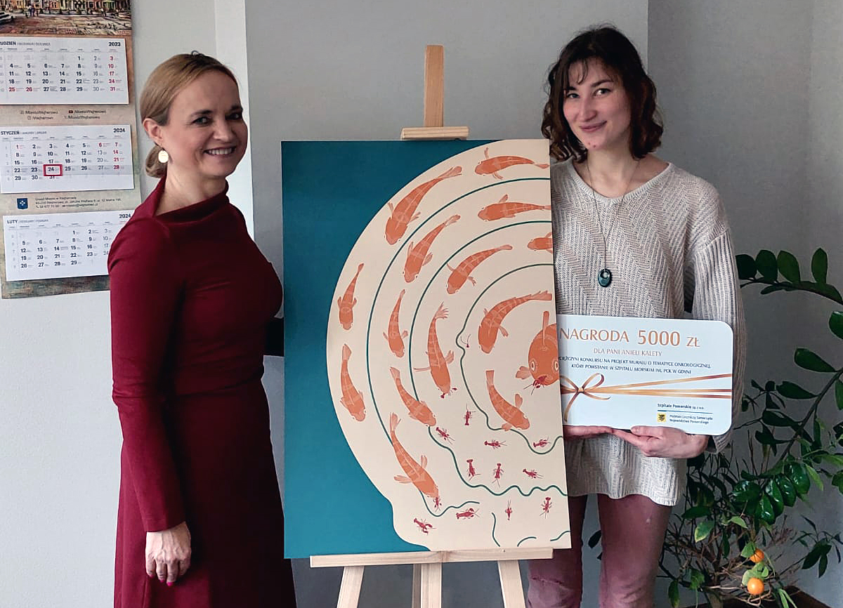 Dwie kobiety stoja przy projekcie muralu, jedna trzyma duży czek.