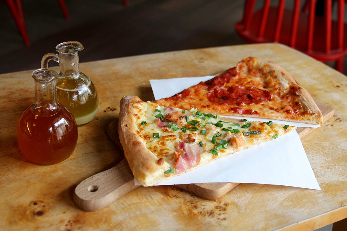 Dwa kawałki pizzy położone na drewnianej desce. Obok oliwa z oliwek w szklanych buteleczkach.// fot. www.kulinarnagdynia.pl