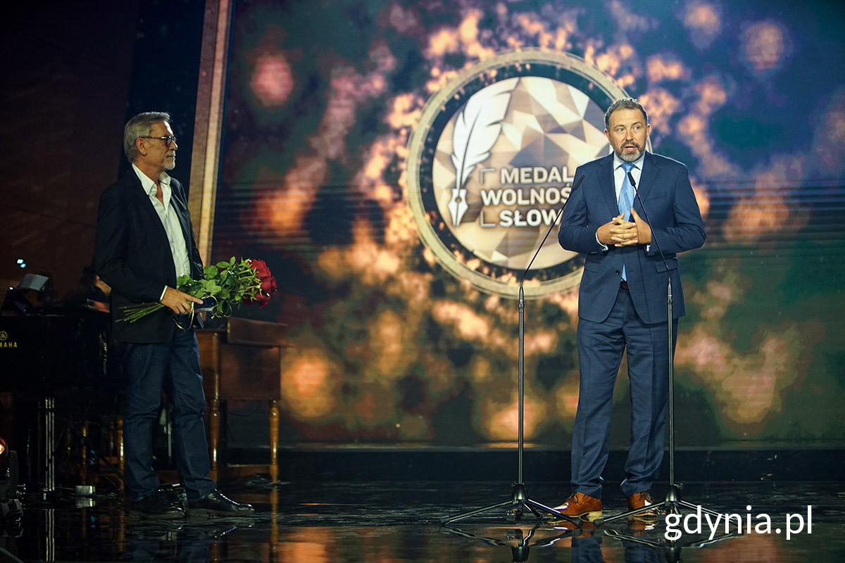 Piotr Świerczek, przemawia na scenie, w tle dekoracja