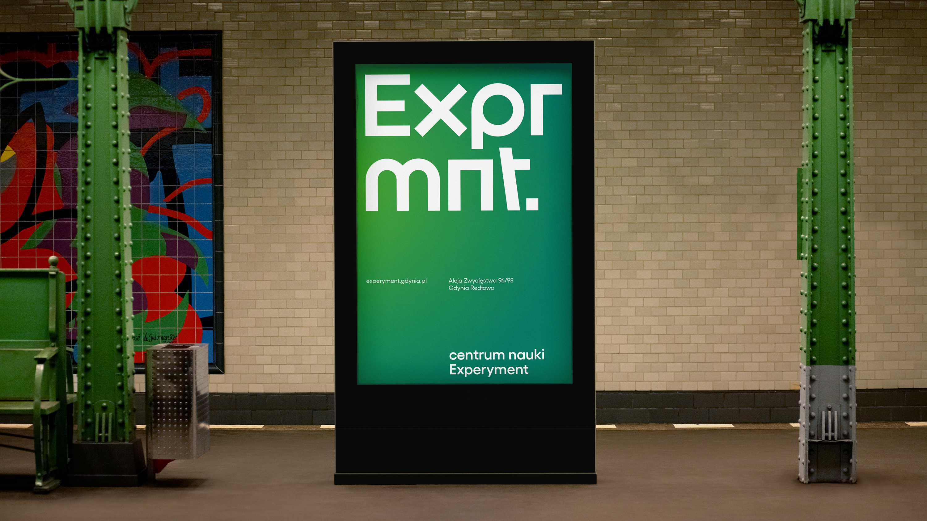 Wizualizacja nowej identyfikacji Experymentu. Na zdjęciu reklama zewnętrzna (outdoorowa). Zielony plakat z dużym białym napisem "Exprmnt." Poniżej, mniejszymi literami napisano: "experyment.gdynia.pl Aleja Zwycięstwa 96/98 Gdynia Redłowo. Centrum Nauki Experyment". Projekt: TOFU Studio // fot. mat. prasowe