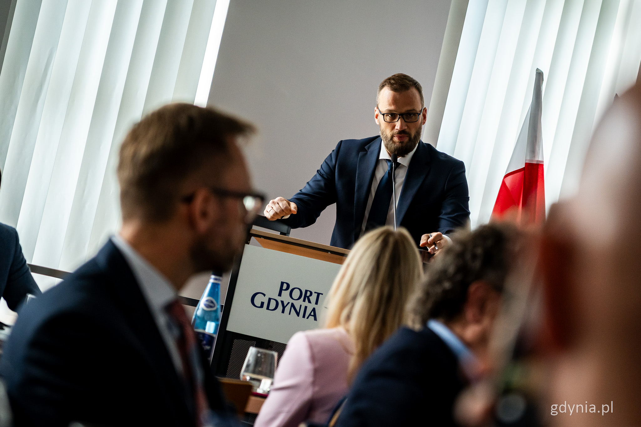 Sala konferencyjna, grupa os&oacute;b, przy m&oacute;wnicy z napisem Port Gdynia przemawia Maciej Samsonowicz